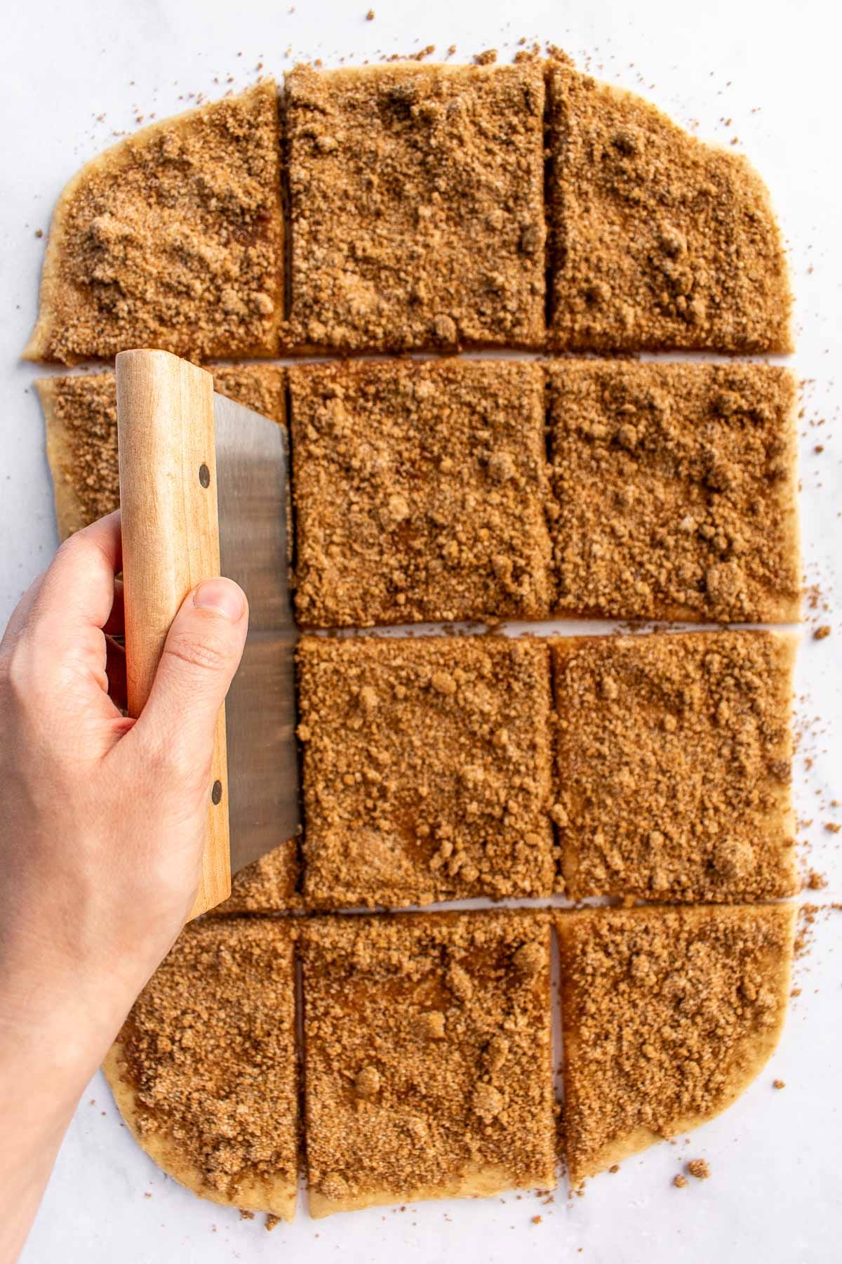 A hand cutting rolled-out dough into twelve squares.