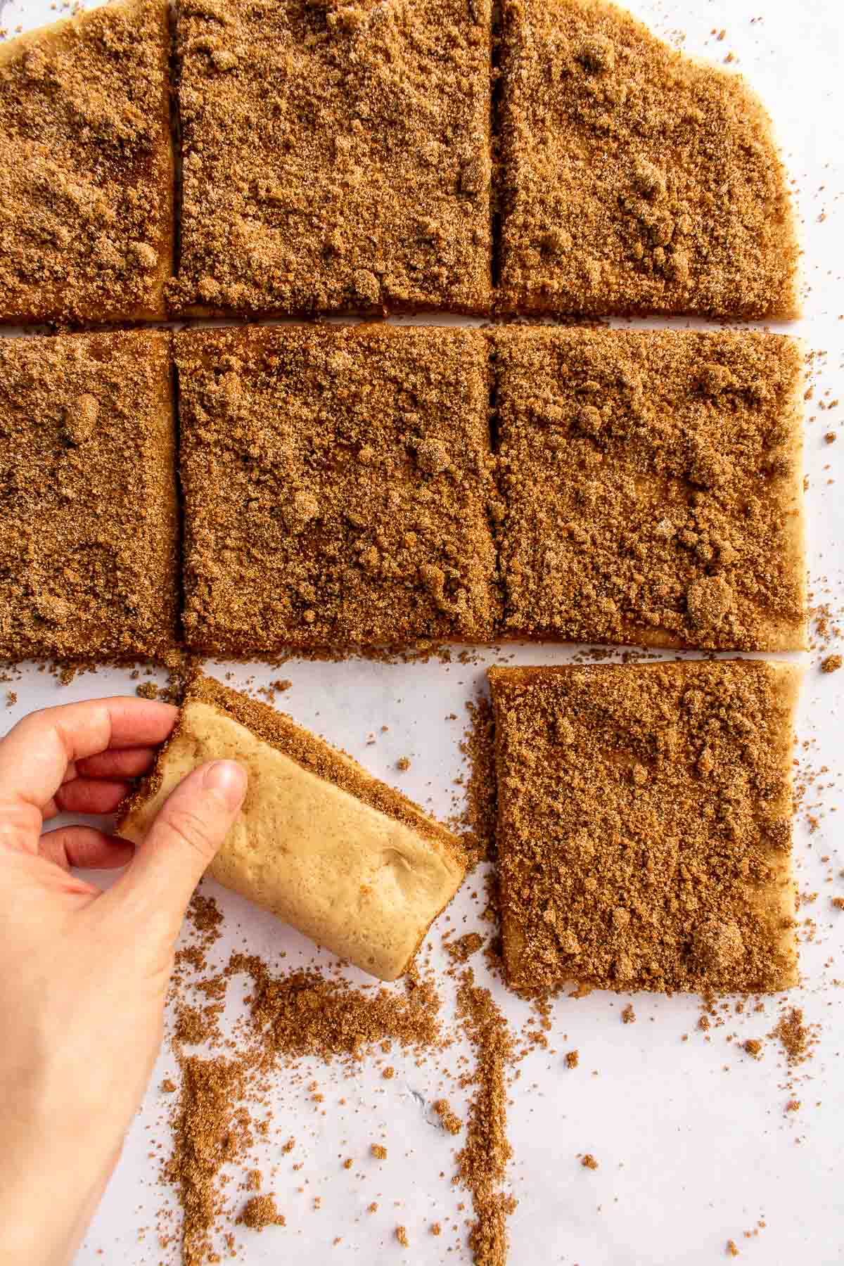 A hand folding squares of sugar-sprinkled bread dough in half.