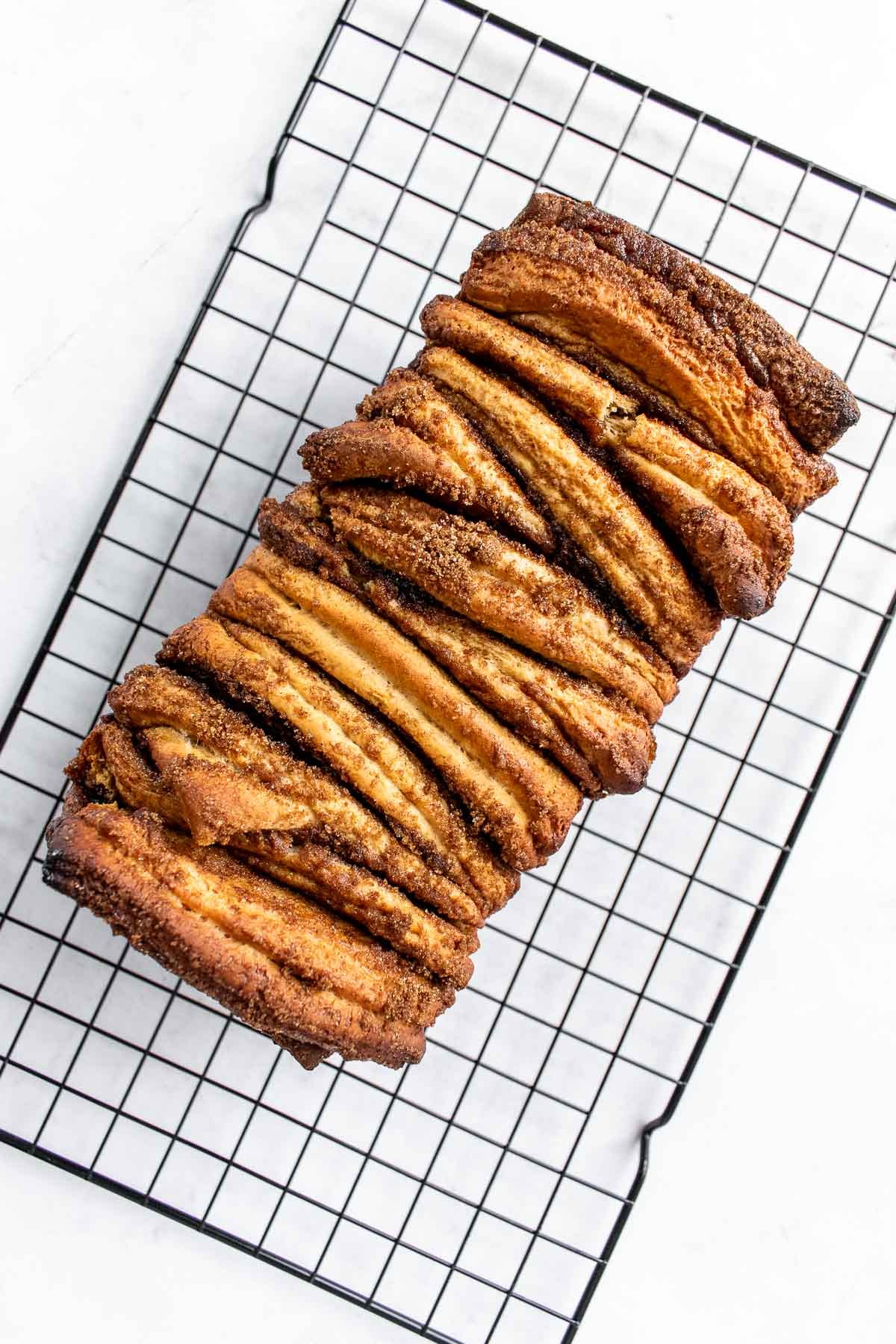 A baked loaf of cinnamon sugar pull apart bread on a cooling rack.