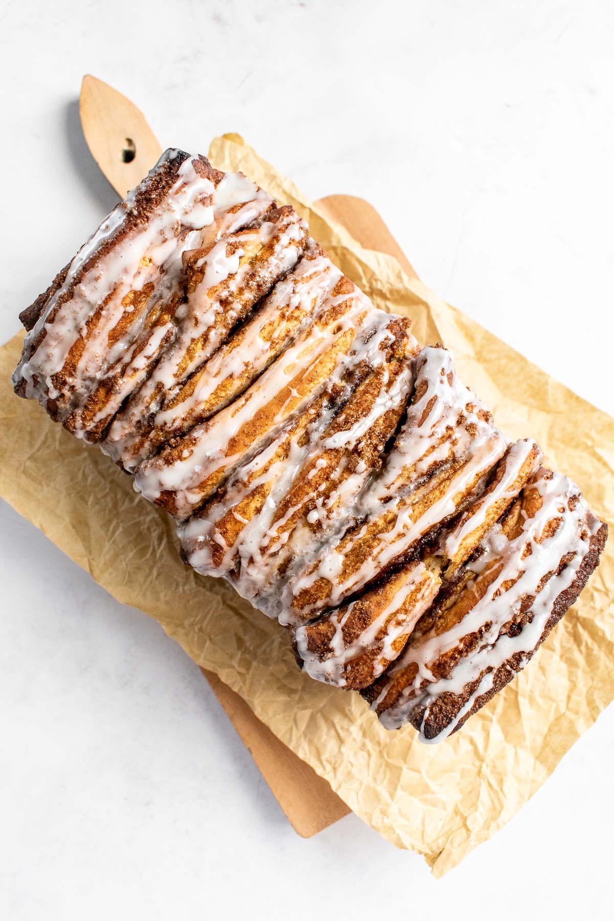 A glazed loaf of sweet pull apart bread on a wood cutting board.