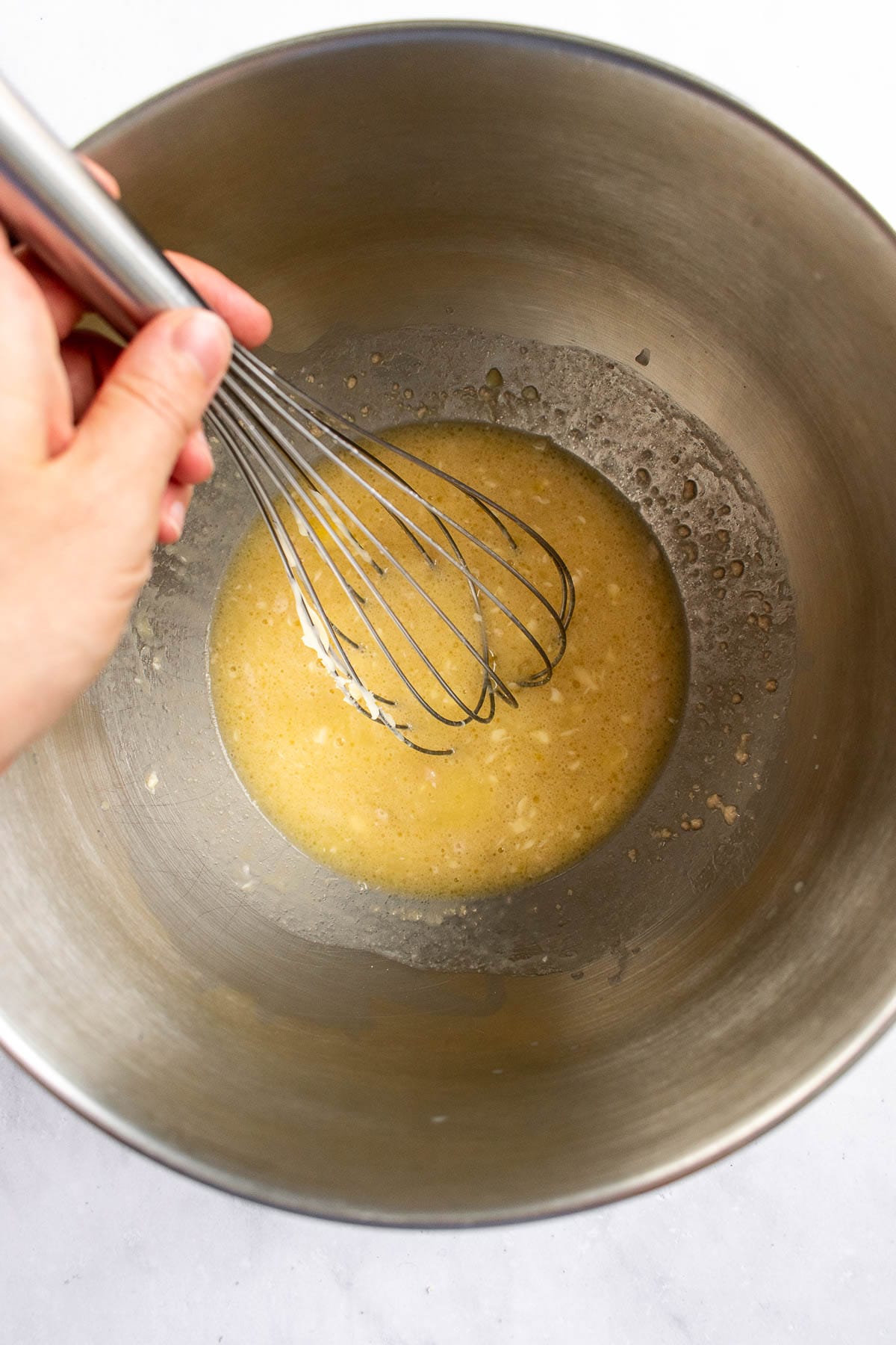 A hand whisking milk, yeast, and sugar in a bowl.
