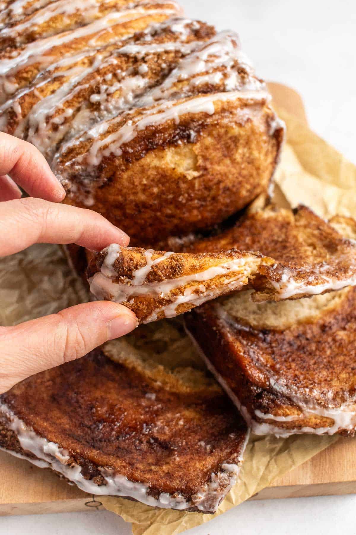 A hand tearing off a slice of cinnamon pull apart bread.