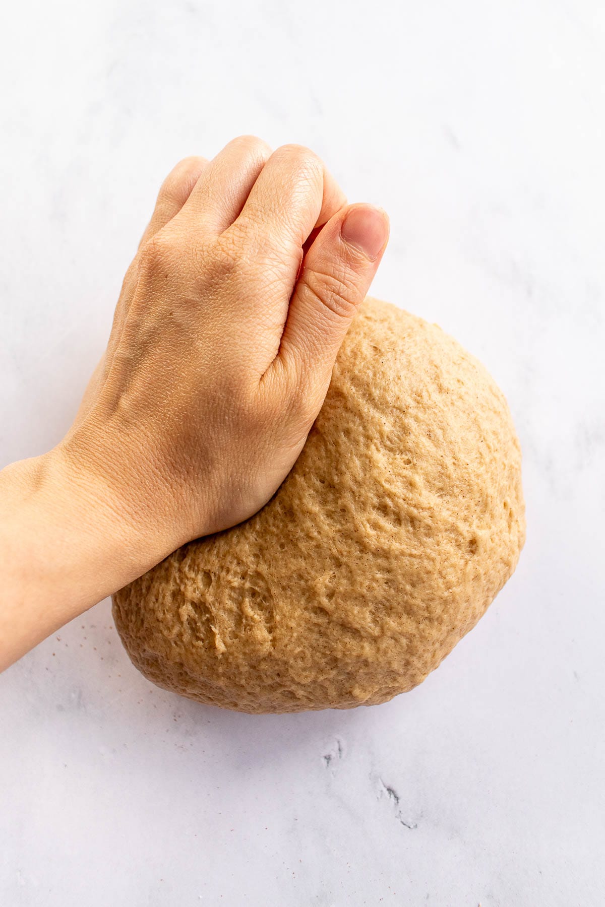 A hand kneading dough on a table.