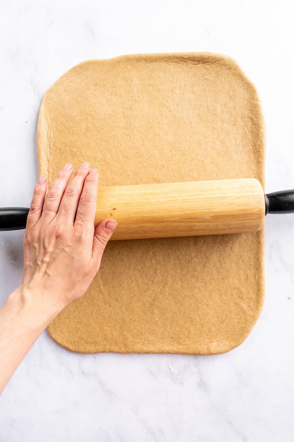 A hand rolling out dough with a wooden rolling pin.