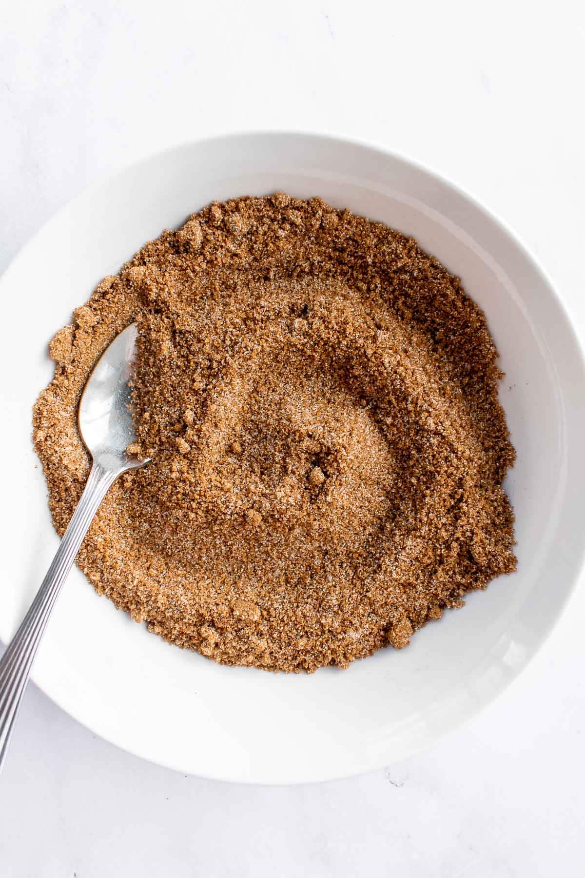 Cinnamon and sugar mixed in a white bowl with a spoon.