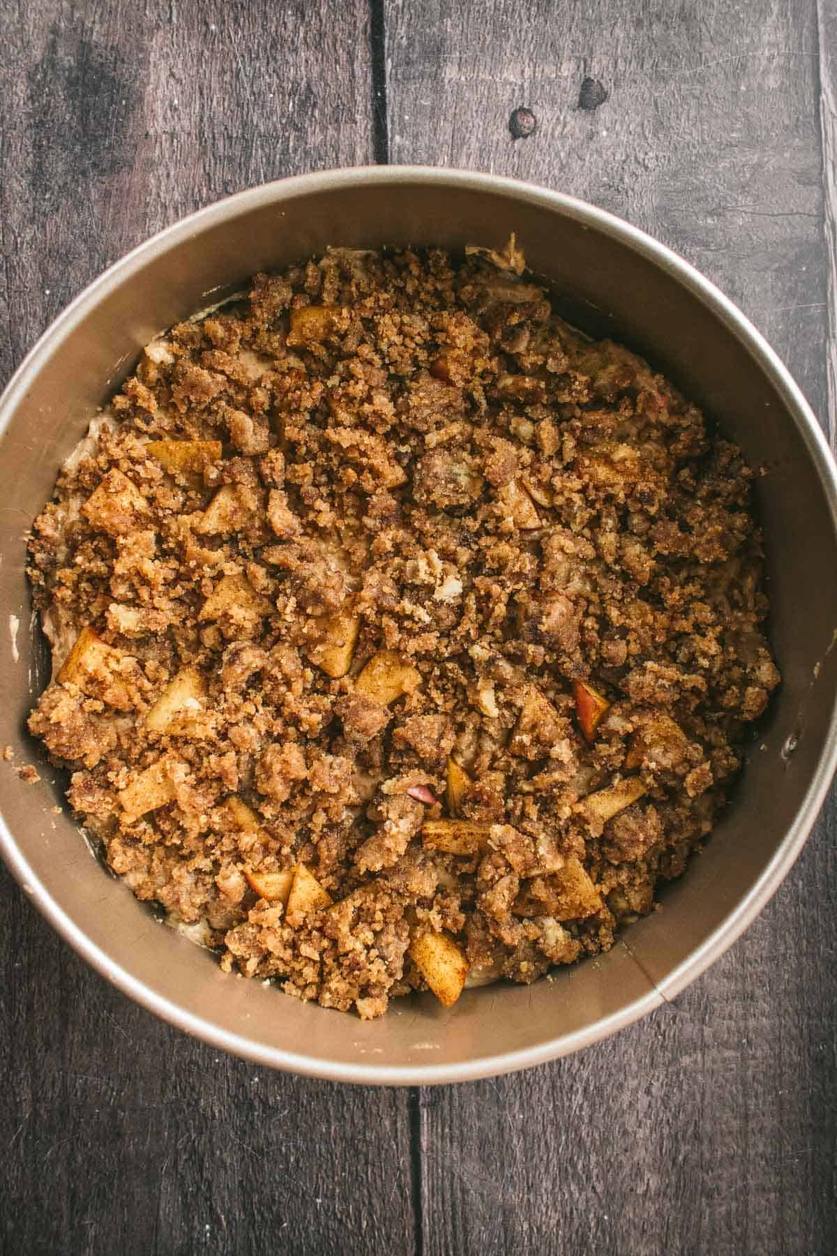 Cake batter in a round tin topped with apples and streusel.