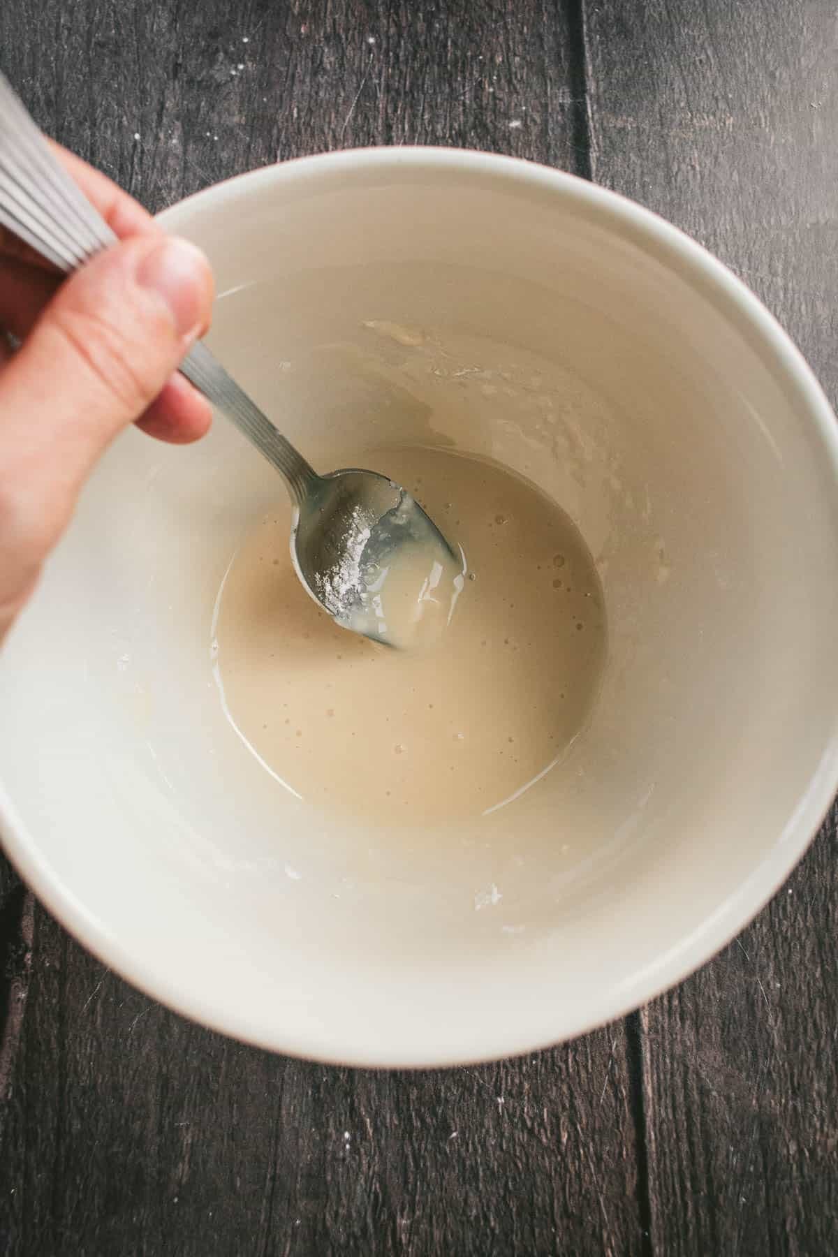 A hand stirring glaze in a white bowl.