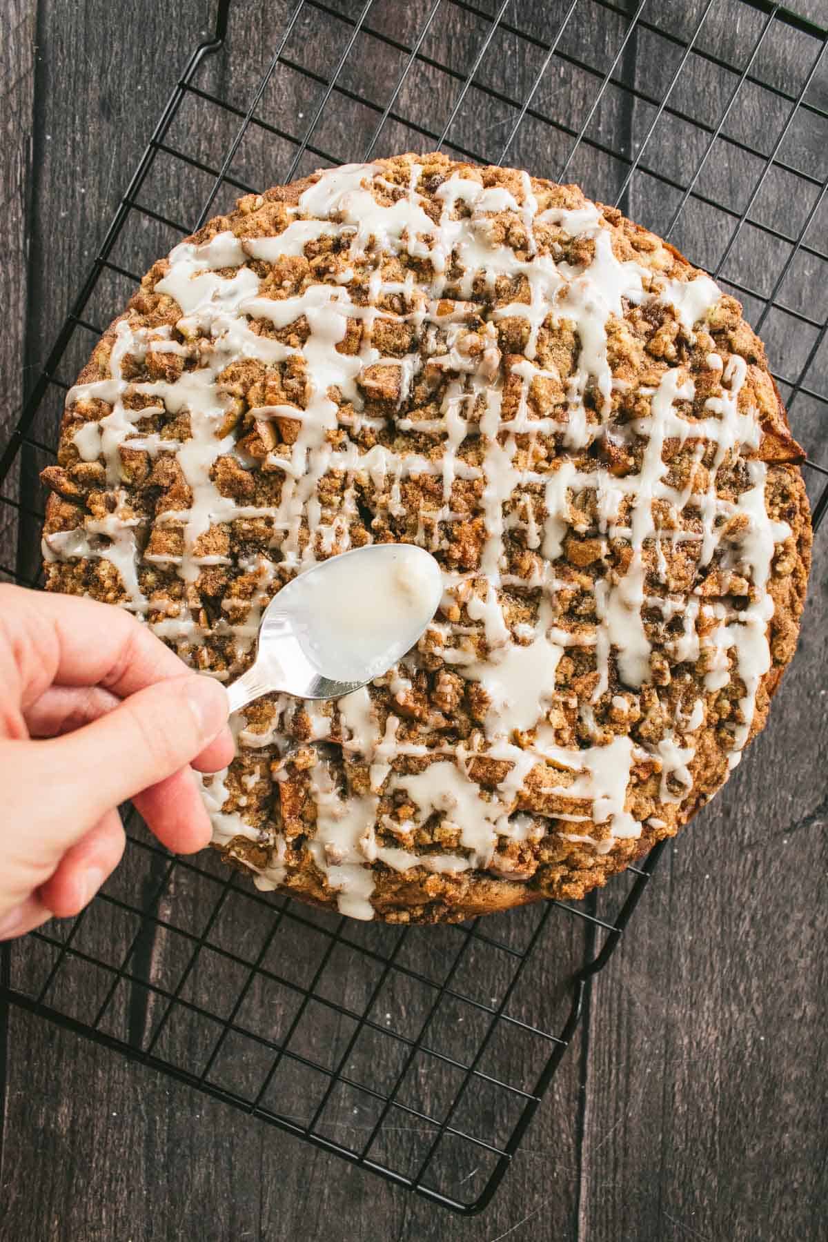 A hand drizzling glaze onto a baked coffee cake.