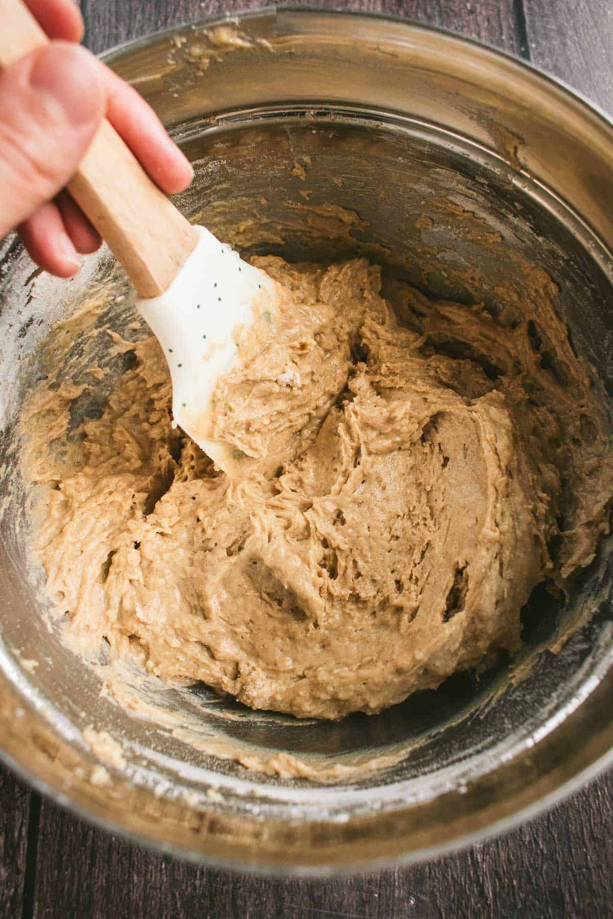 A hand mixing beige cake batter in a metal bowl.