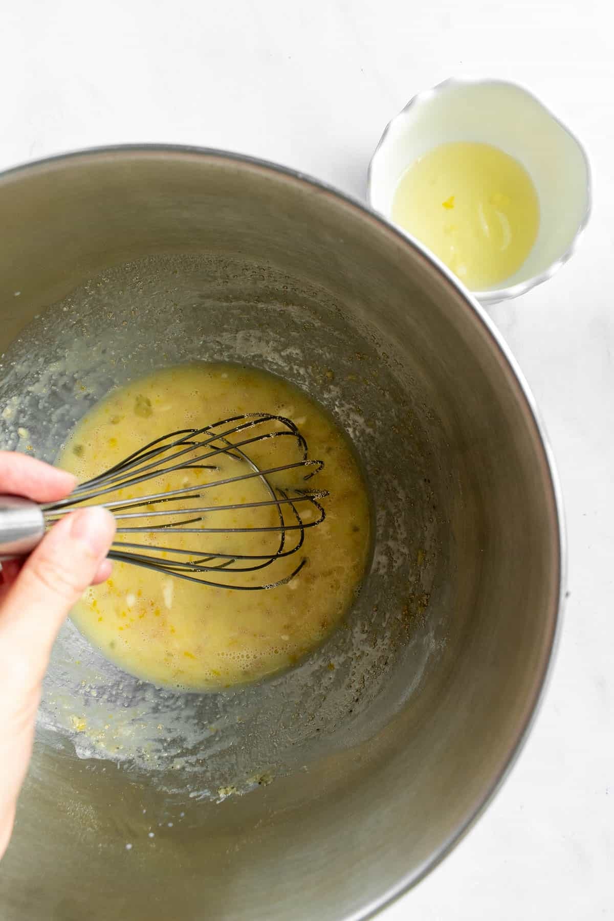 A hand whisking butter, milk, eggs, yeast, and sugar in a large metal bowl. 