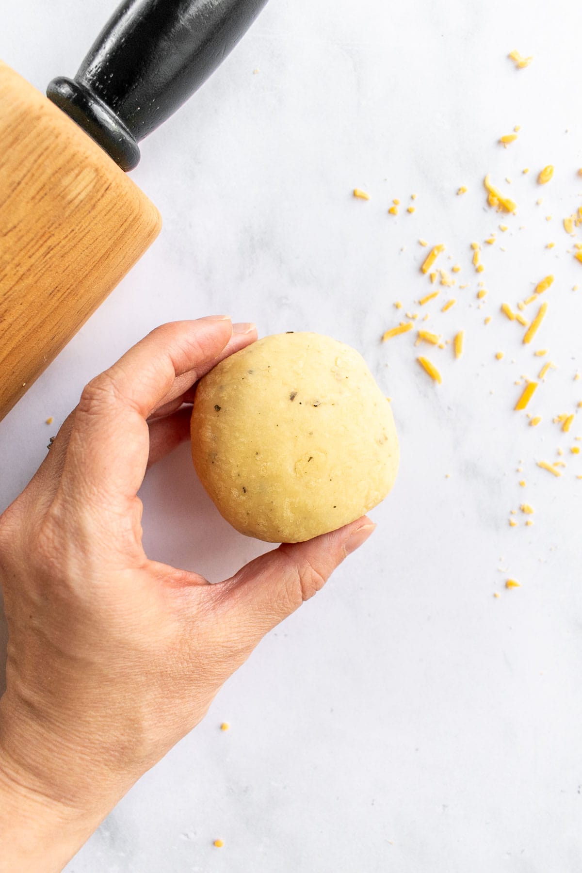 A hand holding a ball of bread dough next to a rolling pin. 