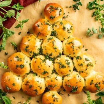 Bread buns topped with chopped herbs and arranged in the shape of a Christmas tree.