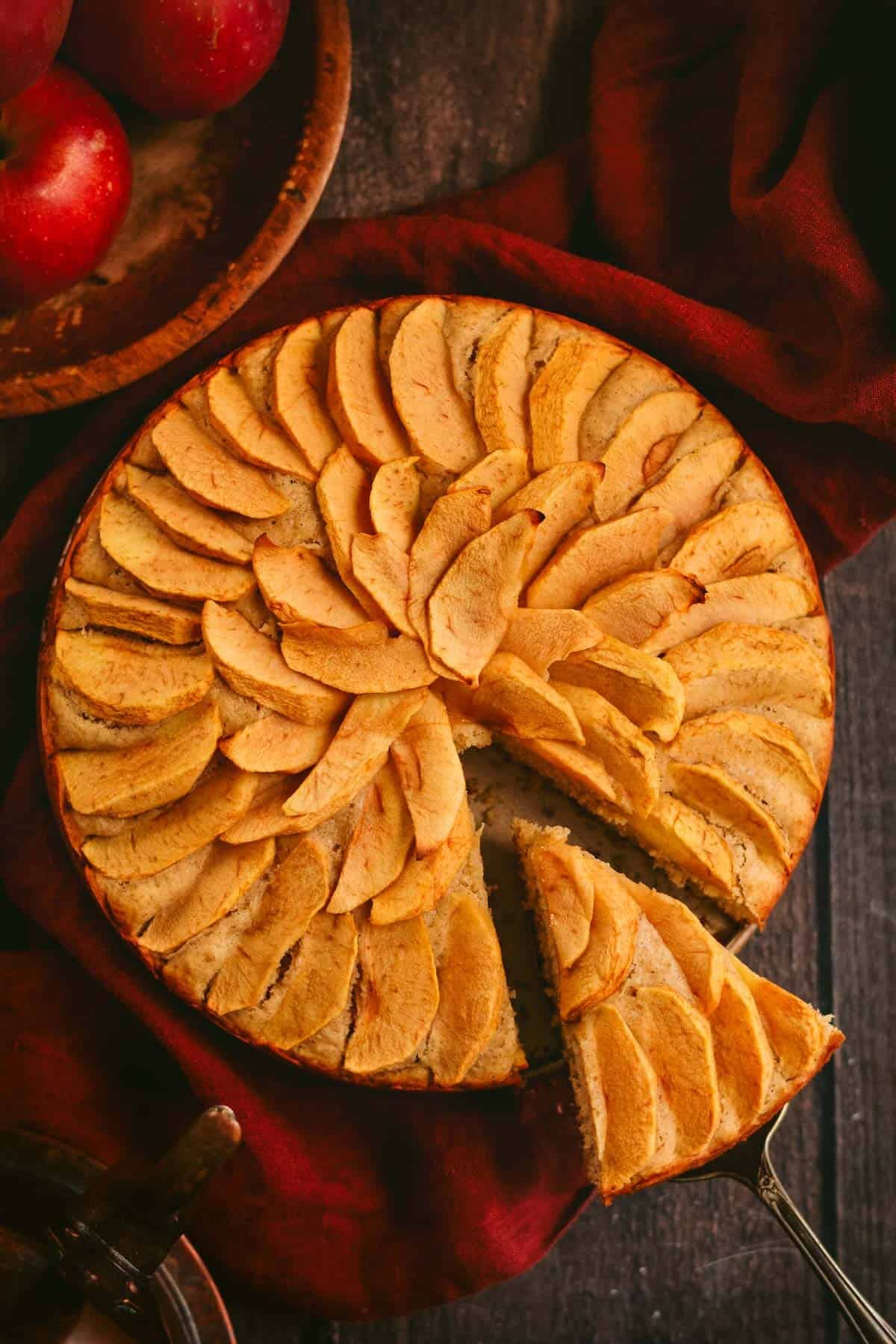An apple cake topped with baked apples with a slice cut out.
