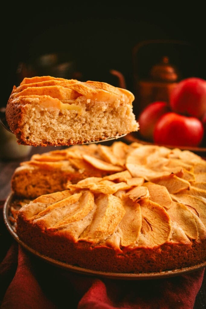 A slice of apple cake on a metal server being lifted from the rest of the cake.