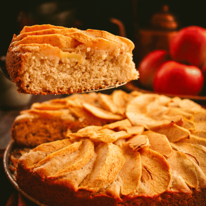 A slice of cake on a metal server over a cake topped with apples.