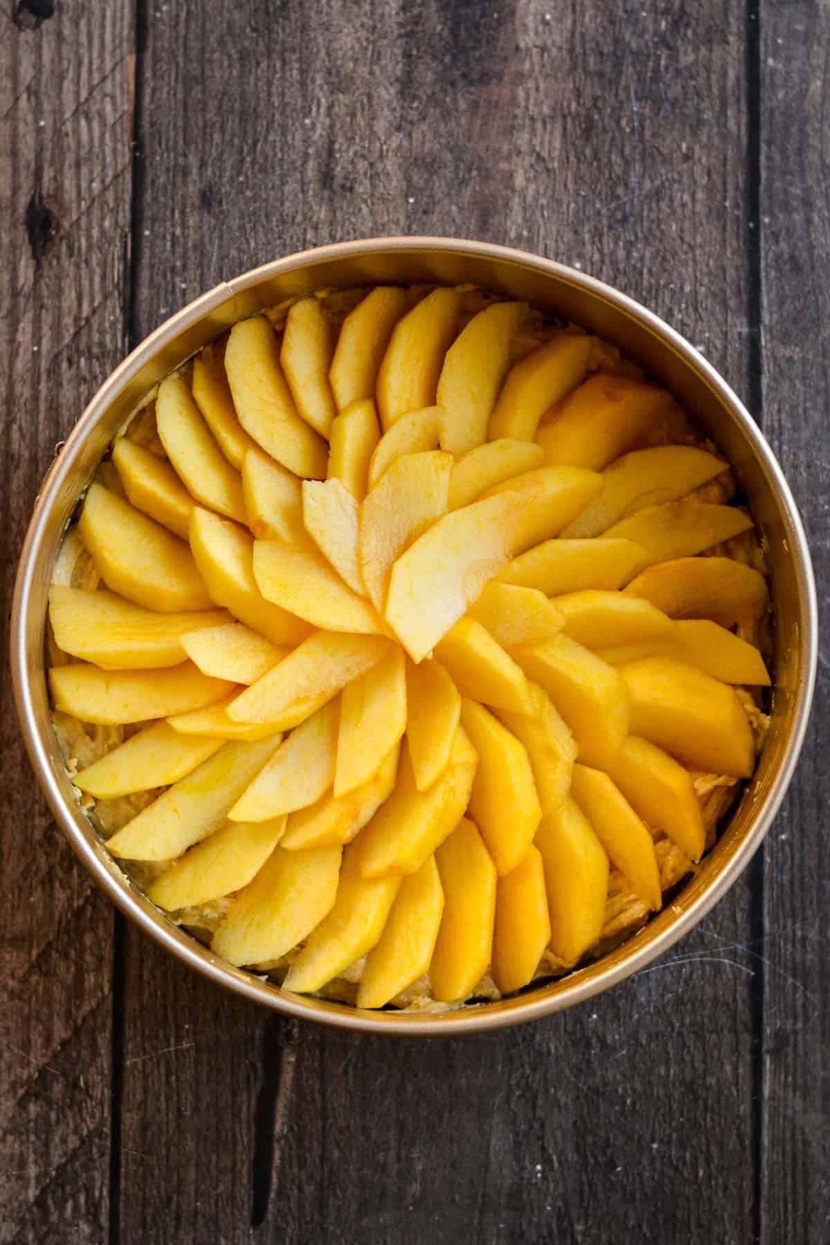 Sliced and peeled apples arranged in concentric circles on cake batter.