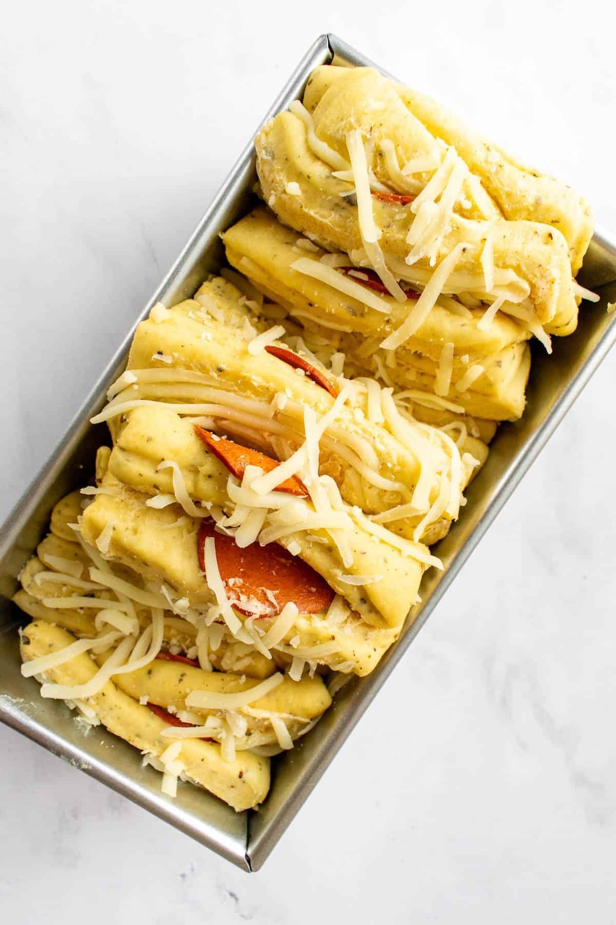 An unbaked loaf of pull apart bread topped with shredded cheese in a loaf pan.