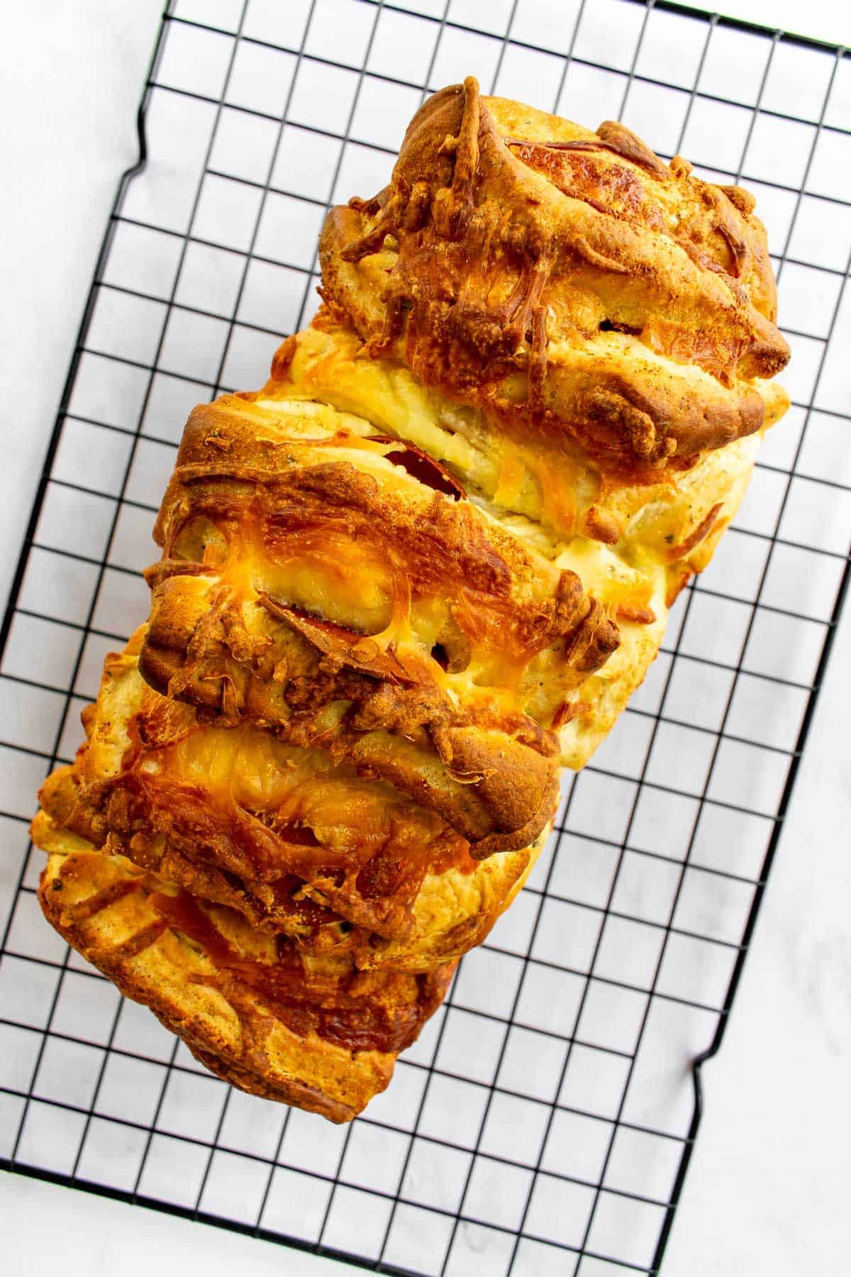 A baked loaf of pizza pull apart bread on a cooling rack.