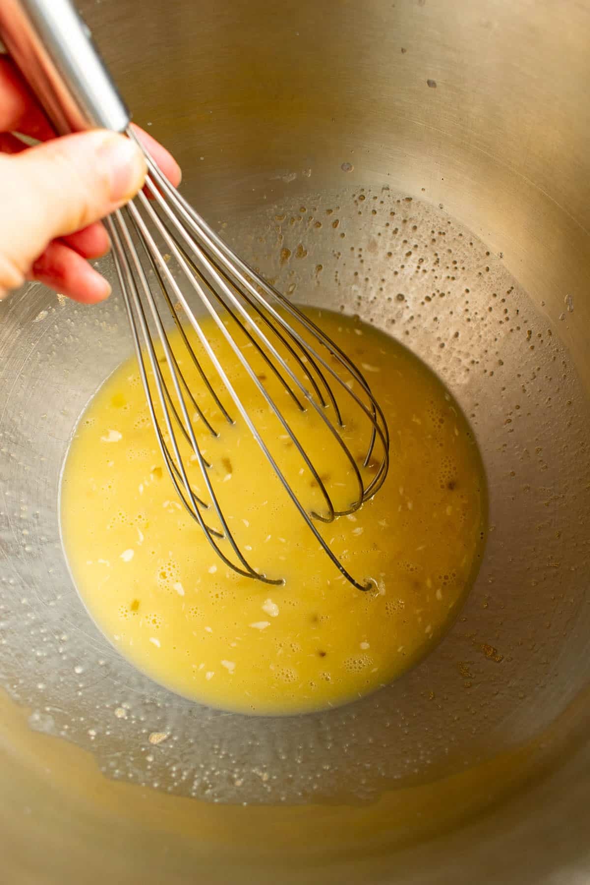 Milk, eggs, butter, and yeast being whisked in a mixing bowl.