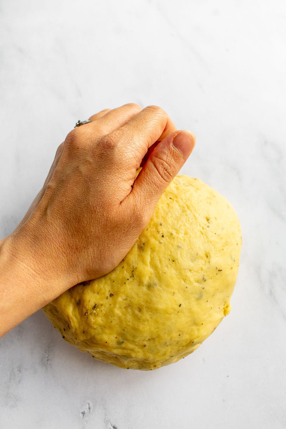 A hand kneading bread dough on a white surface.