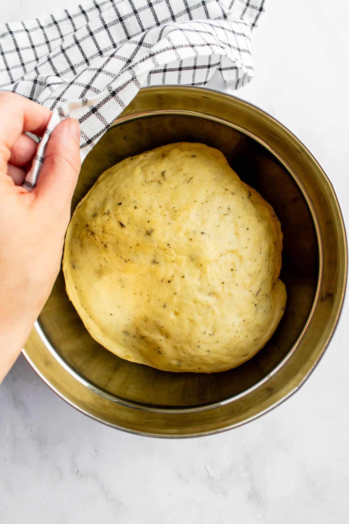 A risen ball of bread dough in a metal bowl.