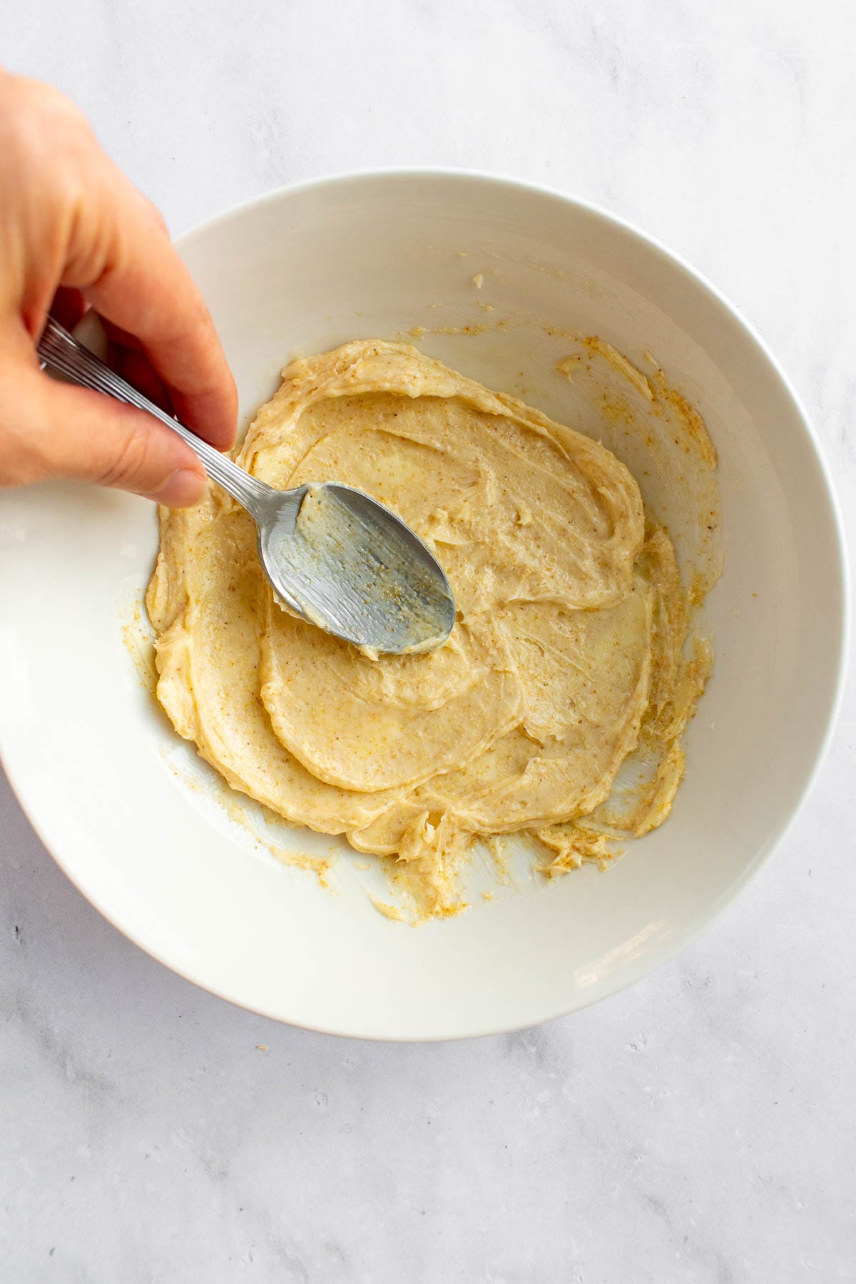 A hand mixing garlic butter in a bowl with a spoon.