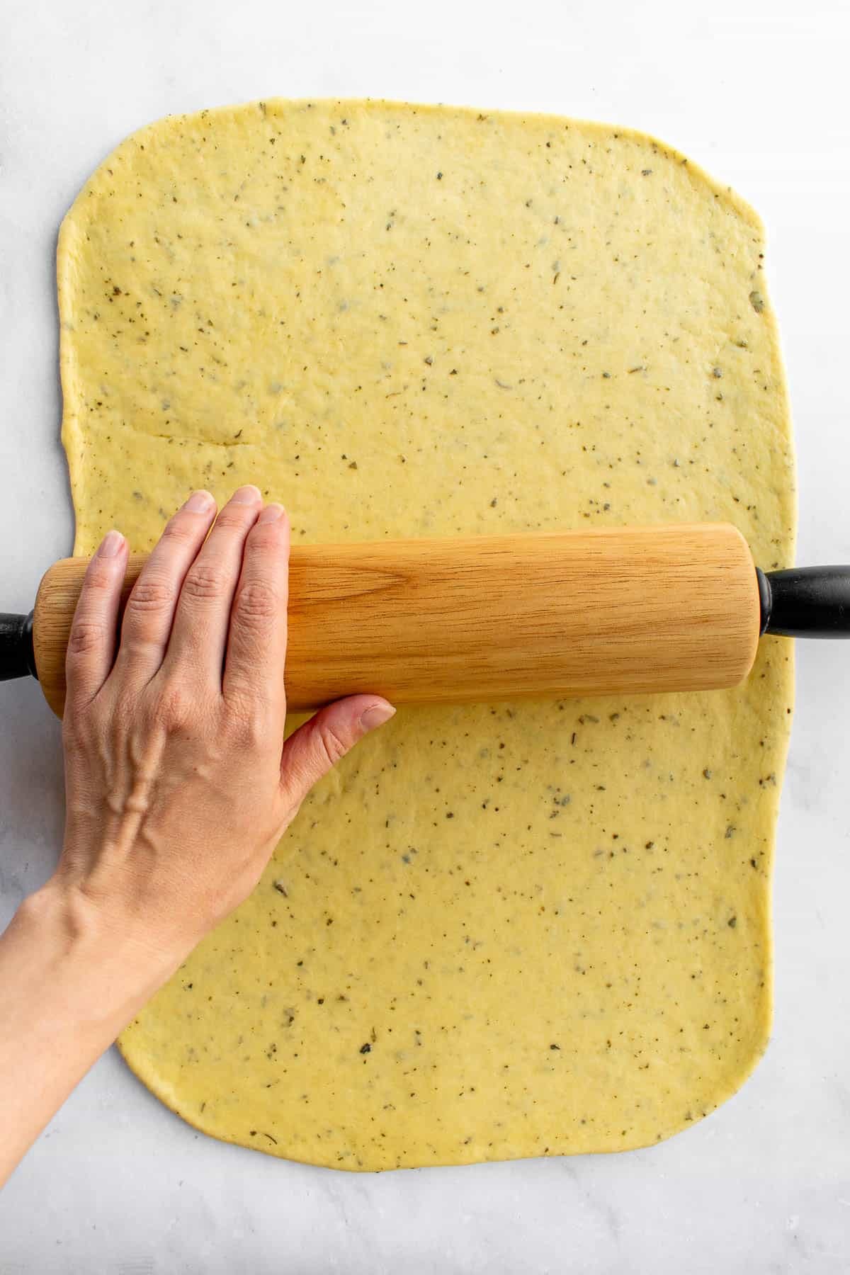 A hand rolling out bread dough with a wooden rolling pin.
