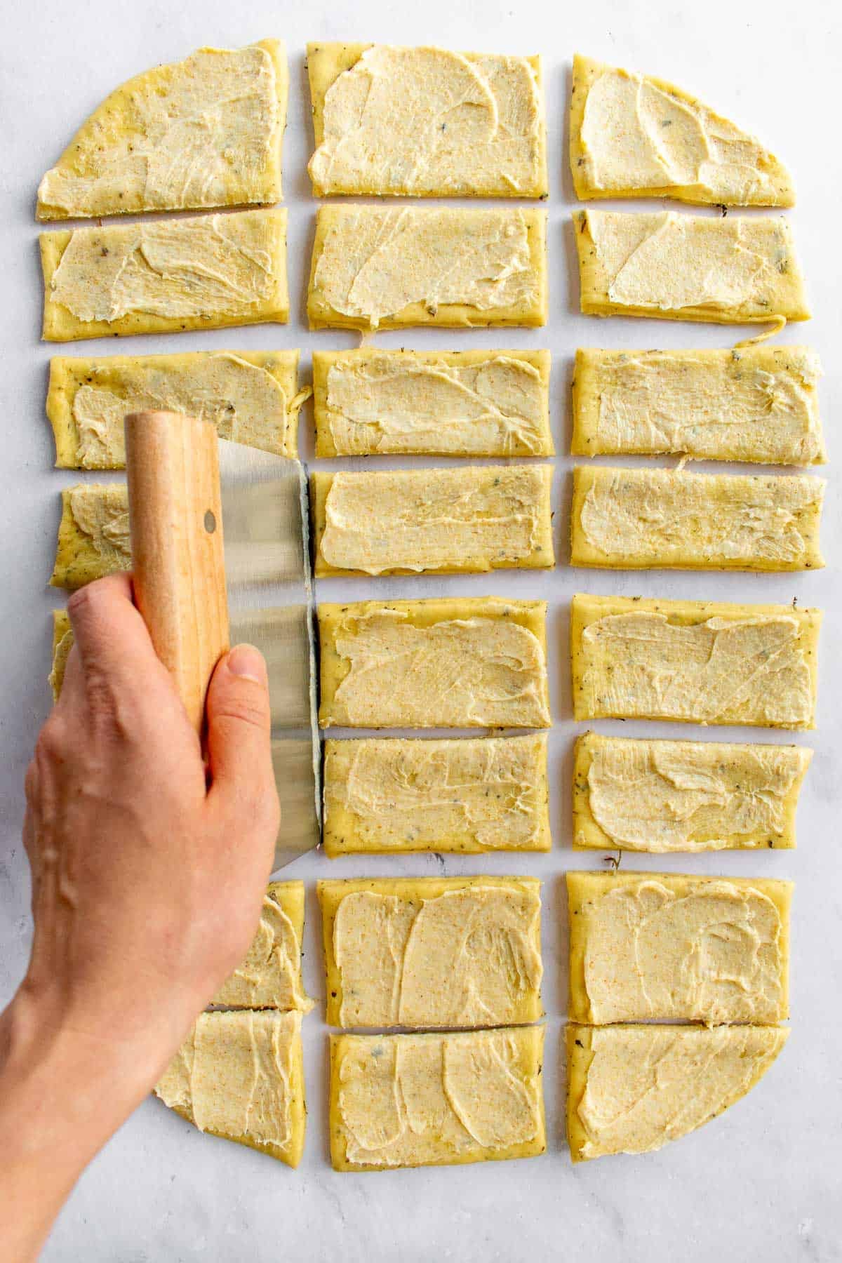 A hand cutting rolled-out bread dough into 16 rectangles.