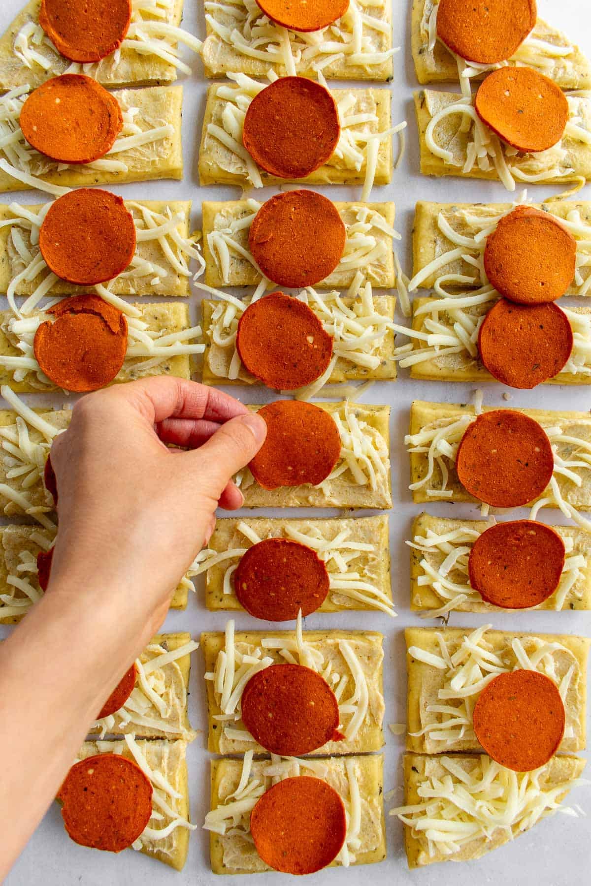 A hand placing pepperoni and shredded cheese on rectangles of bread dough.