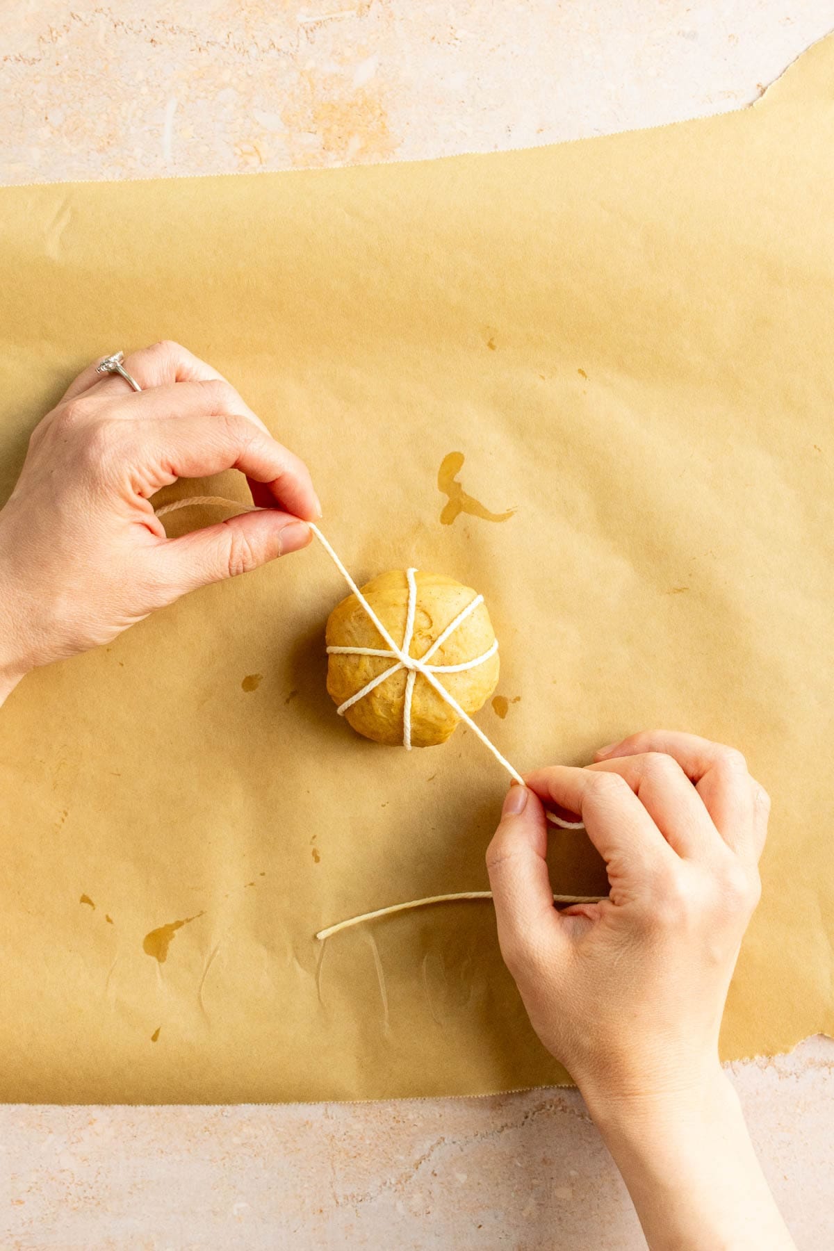 Hands tying baking string around a small ball of bread dough.
