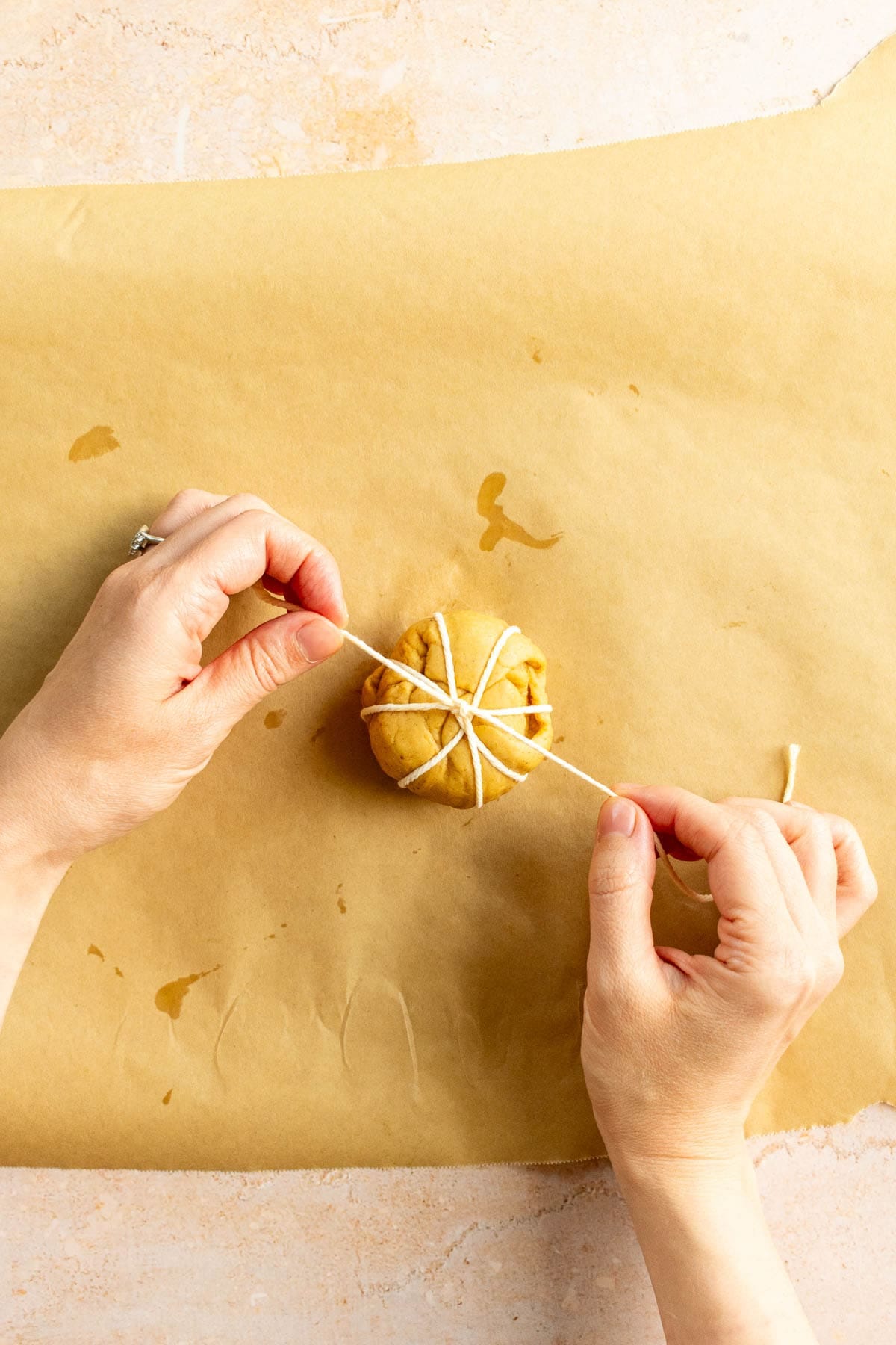 Hands tying baking string around a small ball of bread dough.