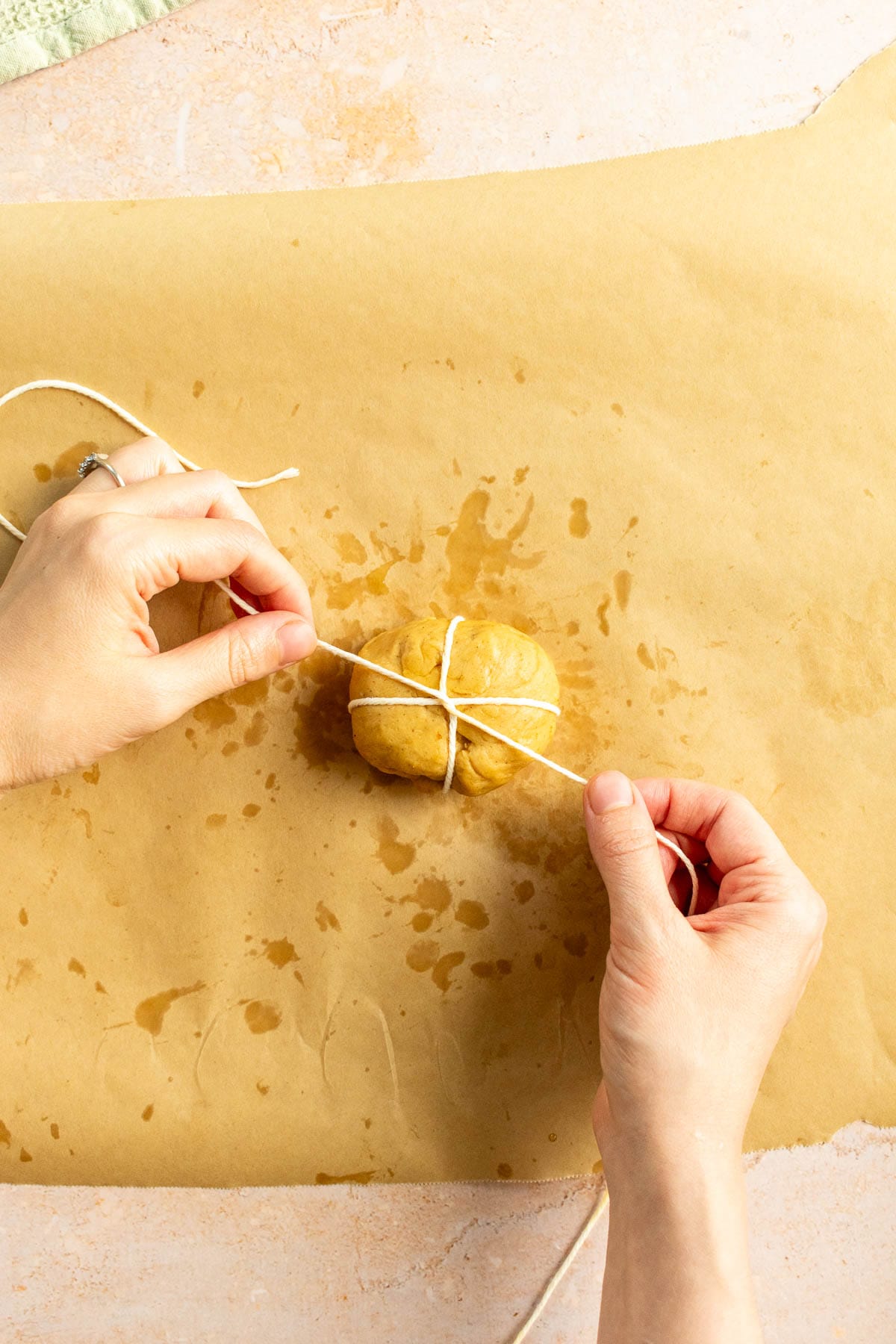 Hands tying baking string around a small ball of bread dough.