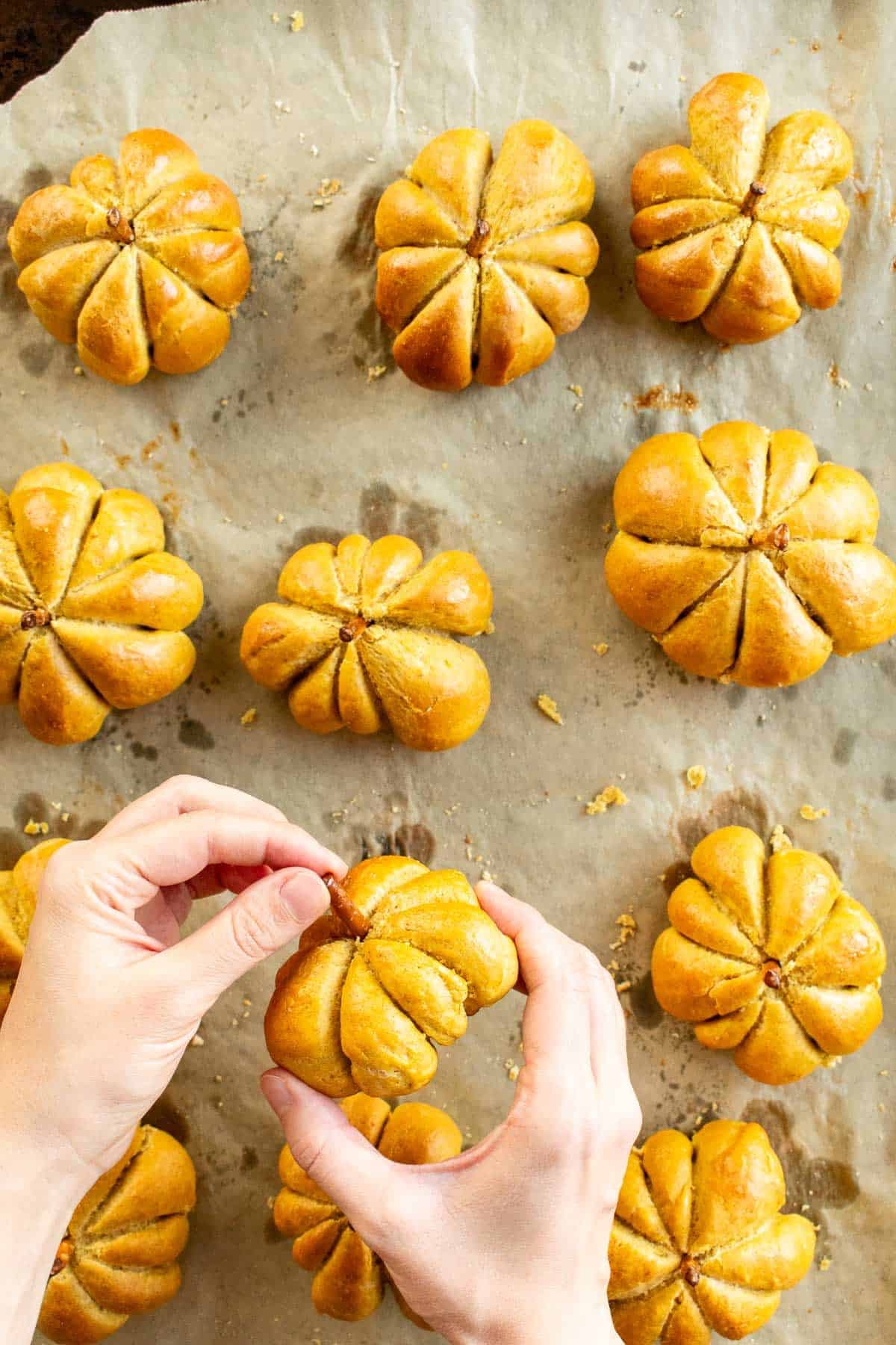 Hand pressing a pretzel stick into the top of a pumpkin shaped bread roll.