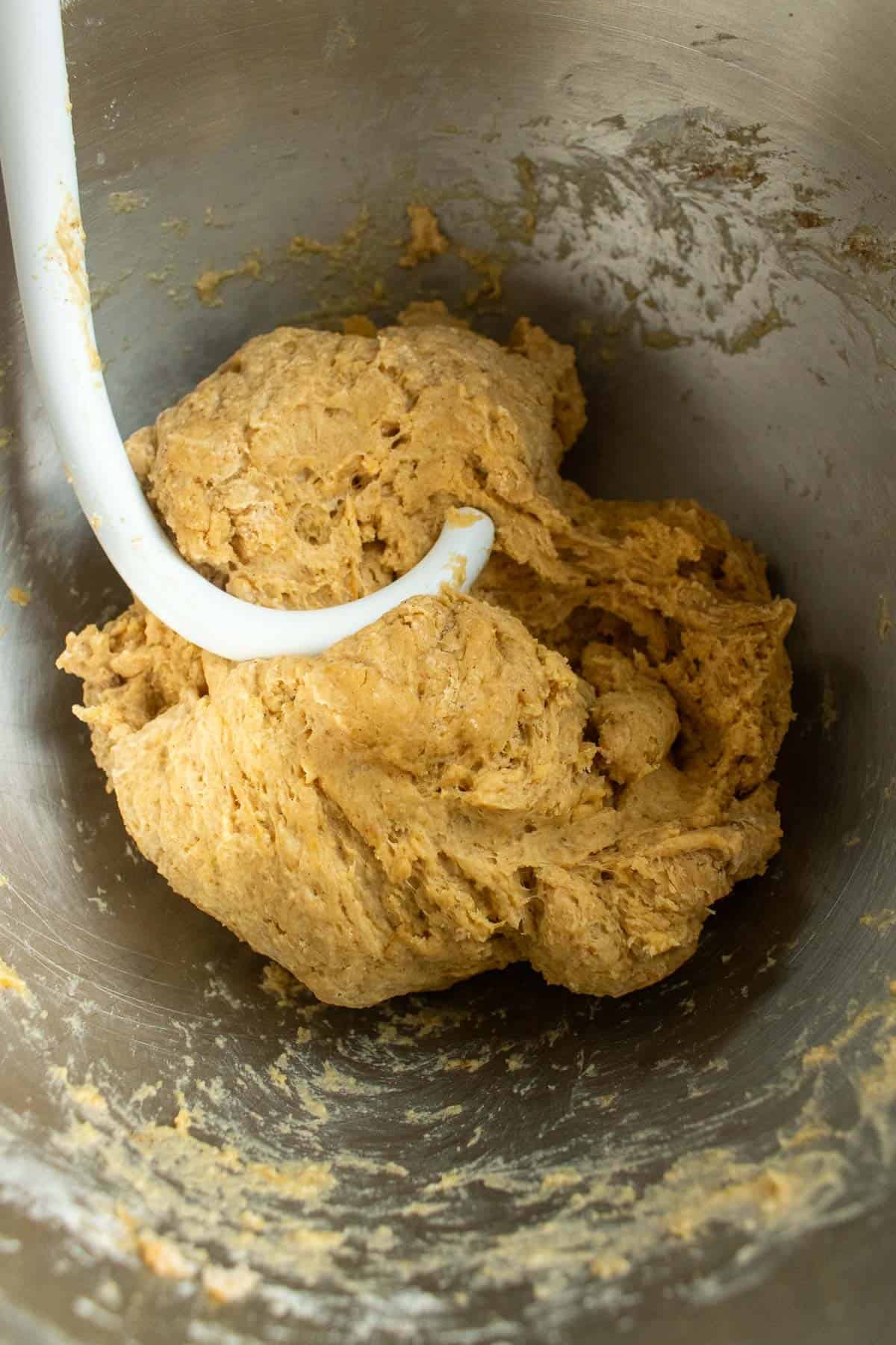 A dough hook in a metal bowl with bread dough.