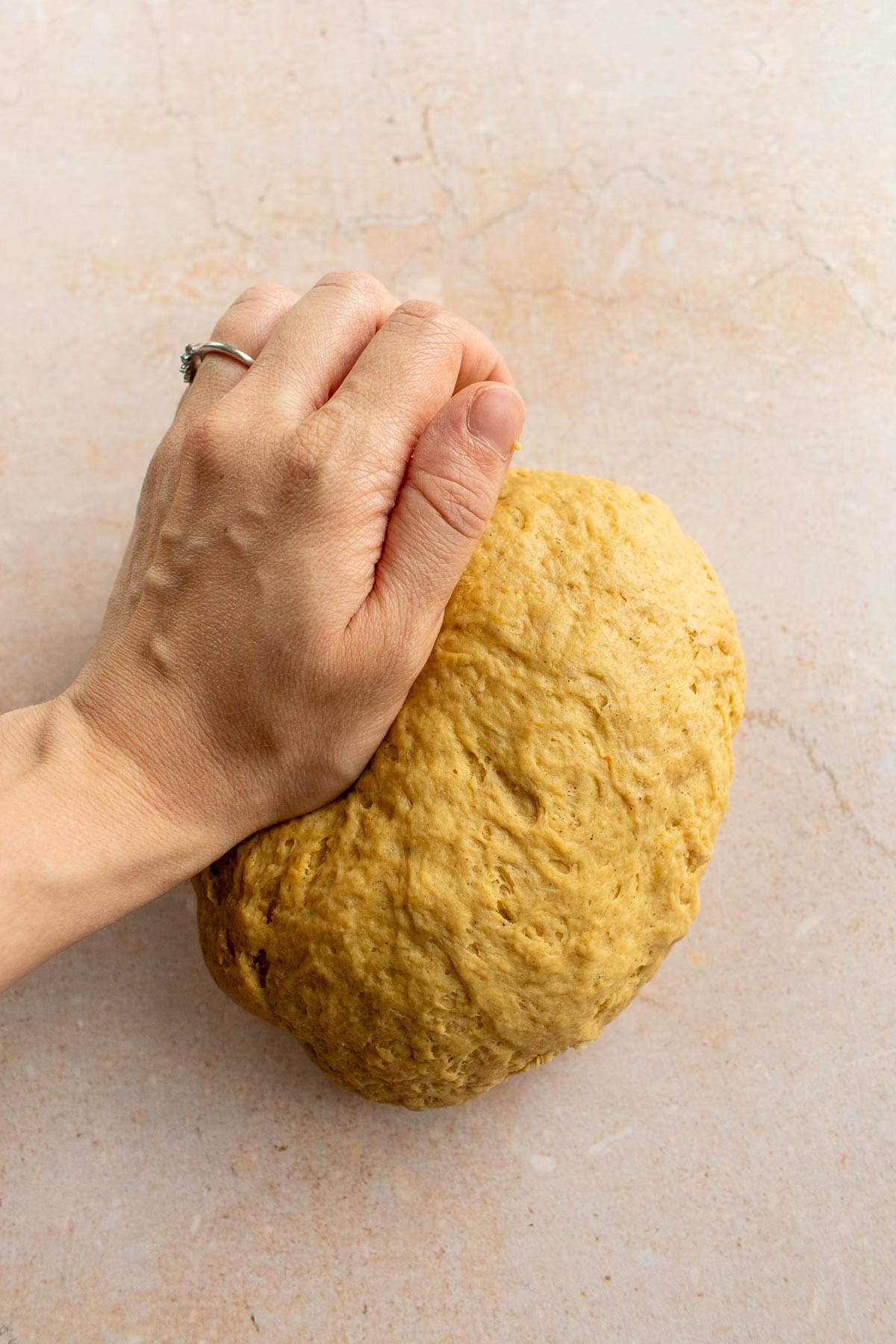 A hand kneading bread dough on a table.