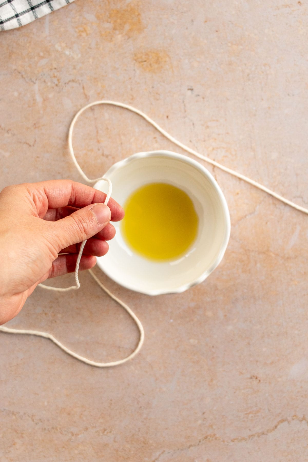 A hand coating baking string in olive oil next to a bowl of oil.