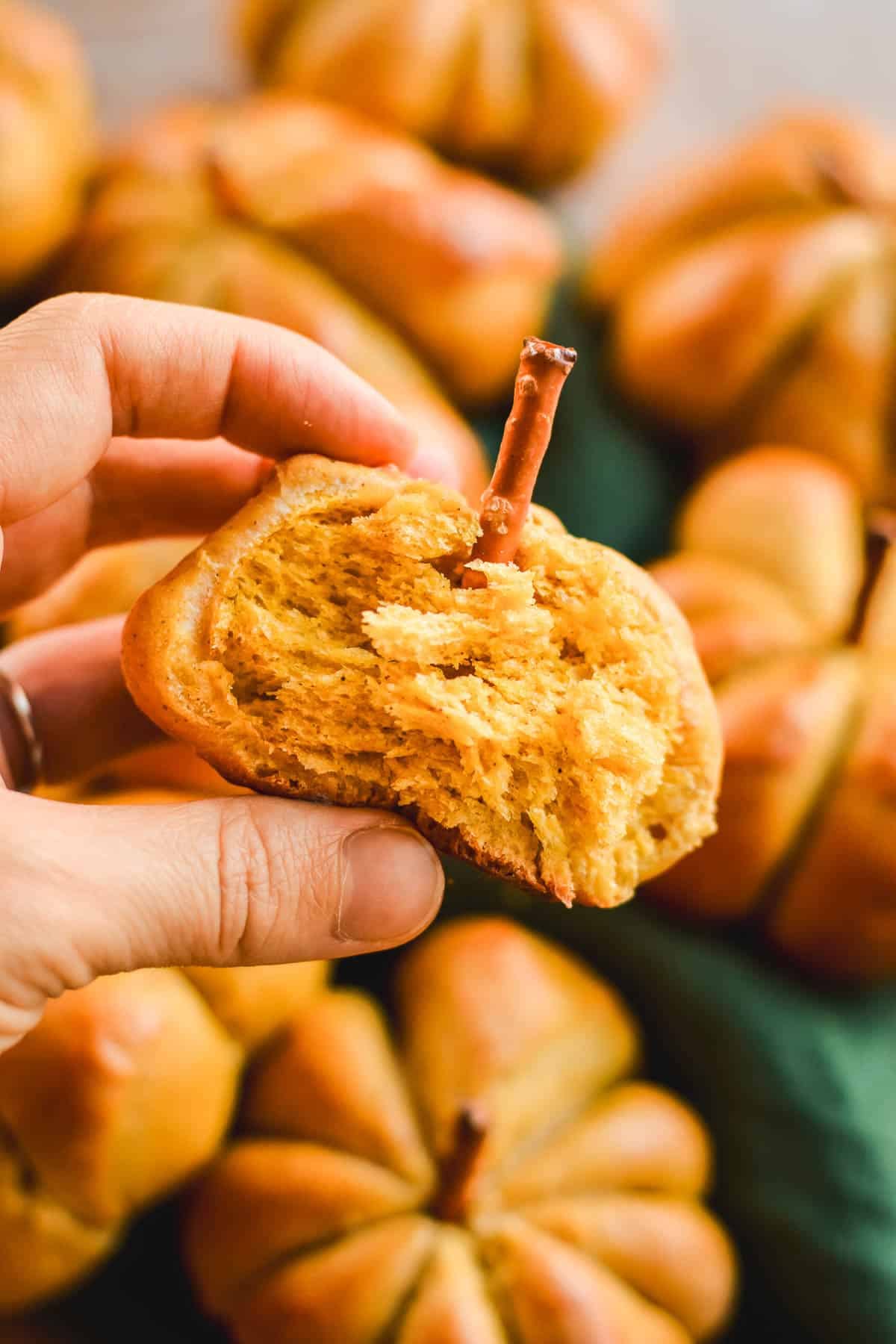A hand holding a half-eaten bread roll shaped like a pumpkin.