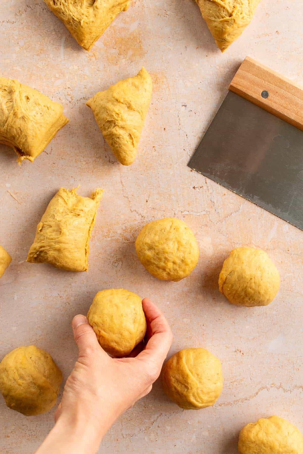 A hand rolling small pieces of bread dough into balls.