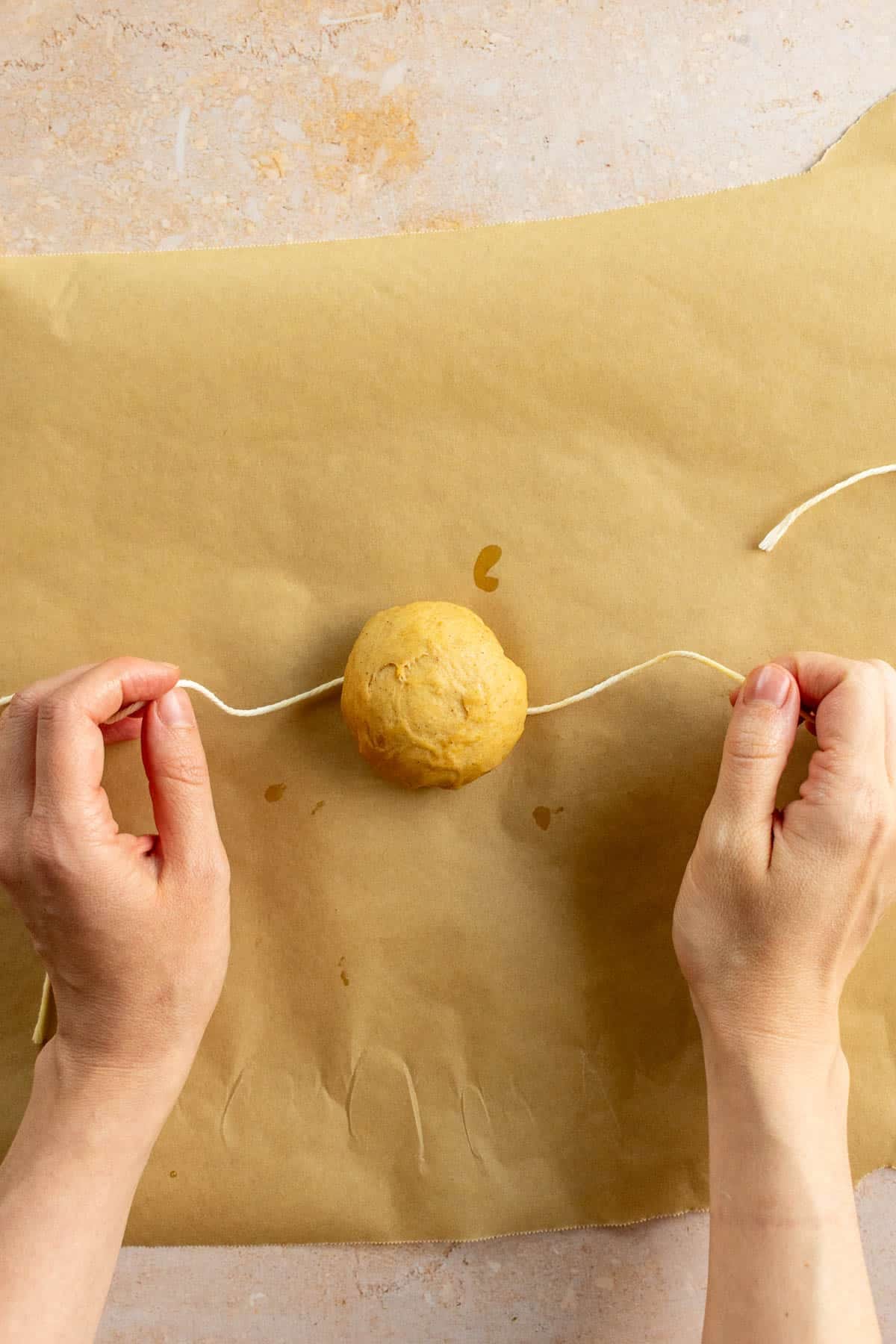 Hands tying baking string around a small ball of bread dough.
