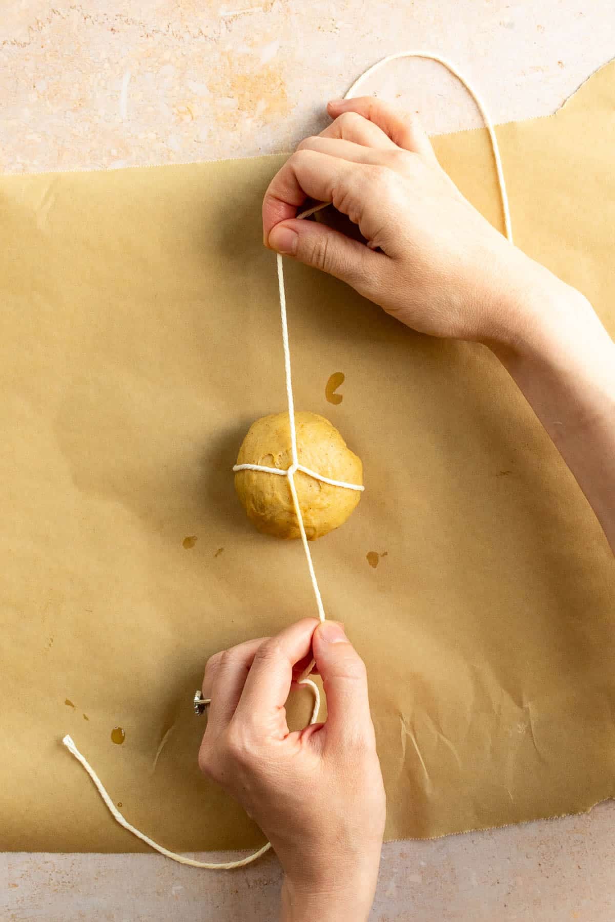 Hands tying baking string around a small ball of bread dough.