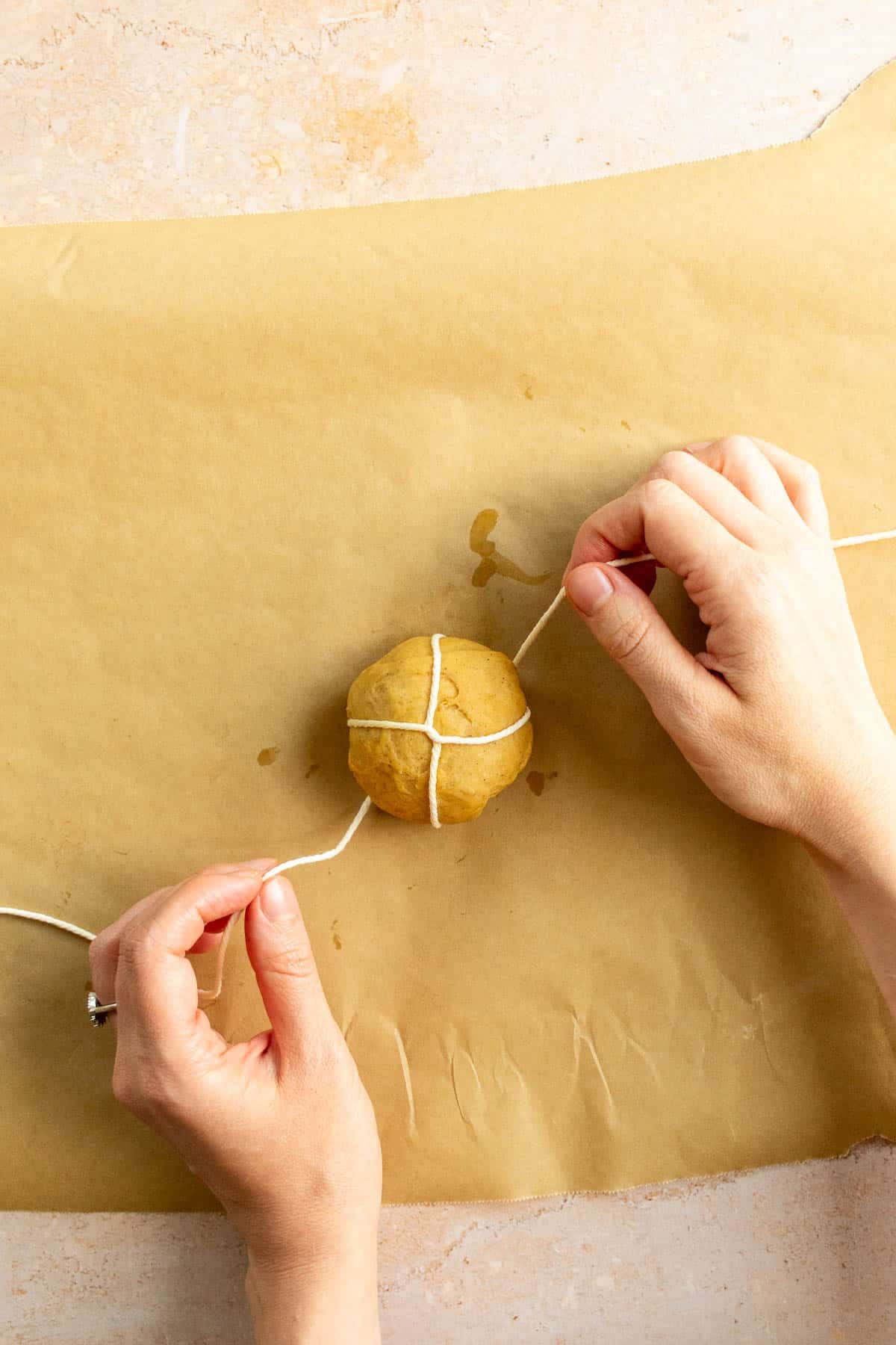 Hands tying baking string around a small ball of bread dough.