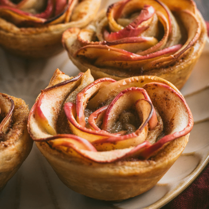 Four apple rose puff pastries on a plate.