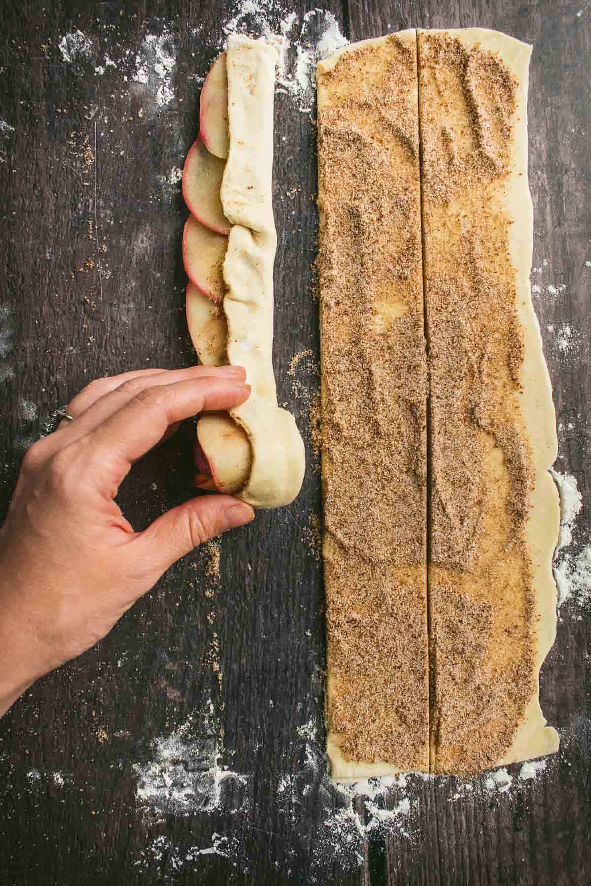 A hand rolling puff pastry dough around apple slices and cinnamon sugar.