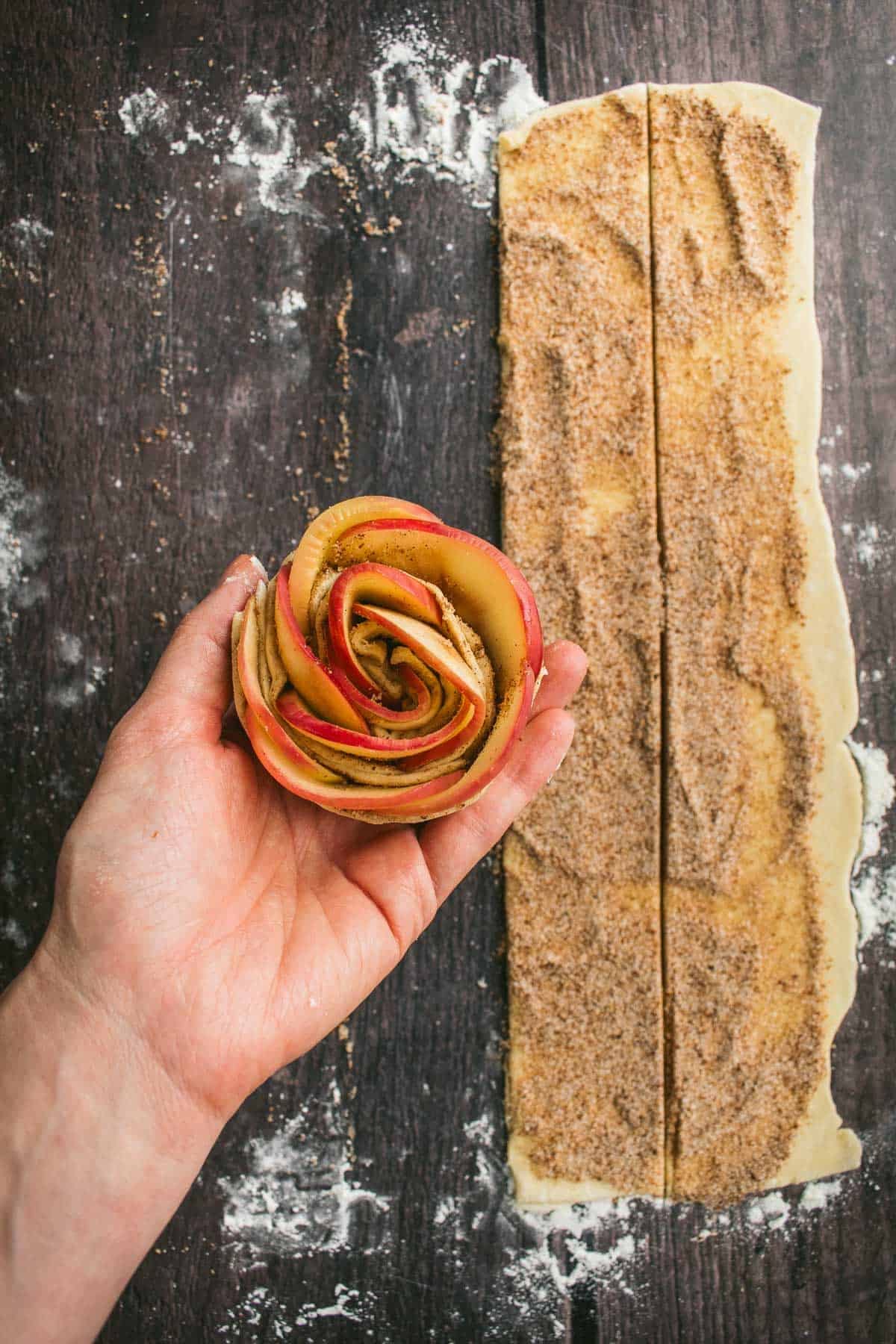 A hand holding an unbaked apple rose puff pastry.