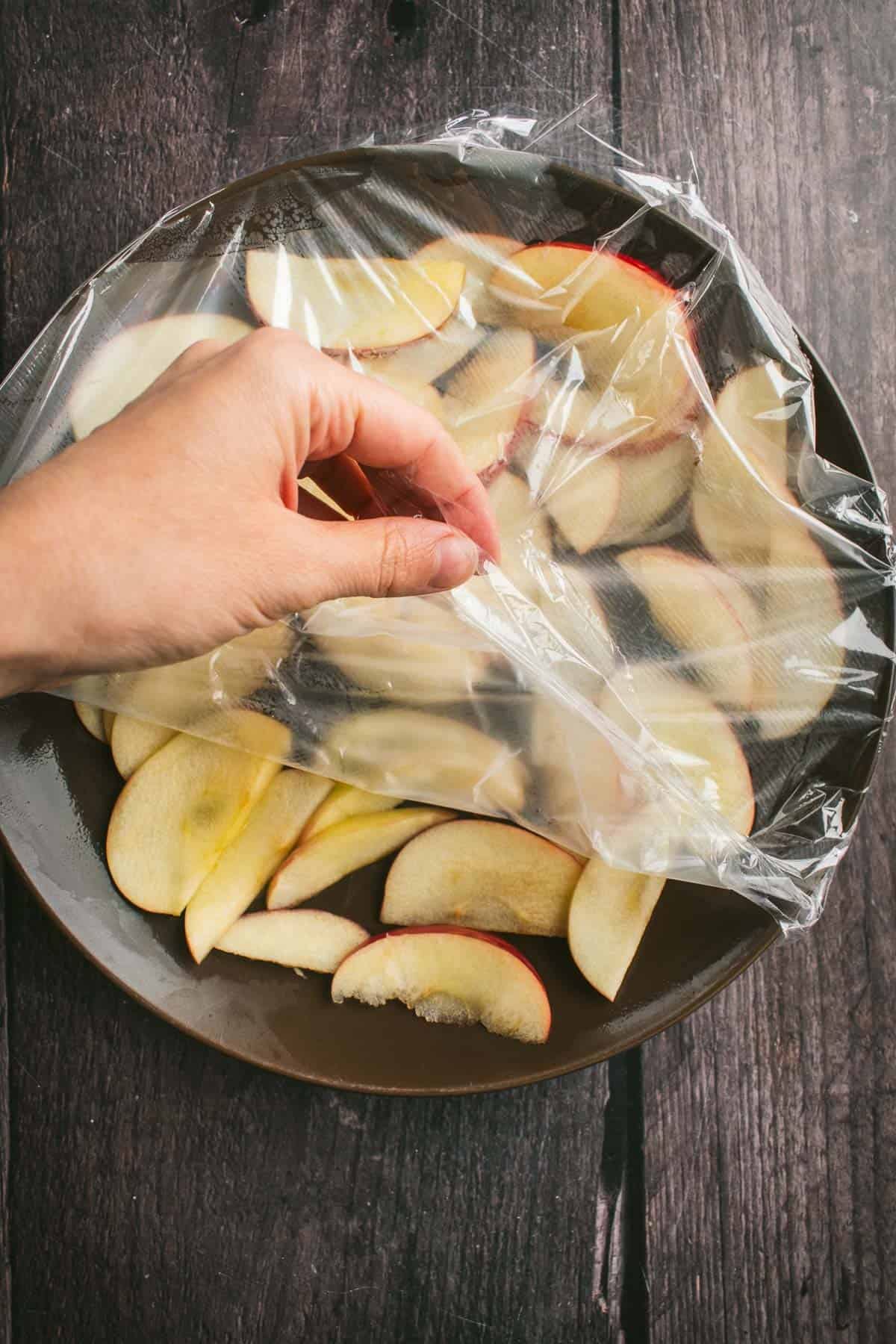 Thinly sliced apples on a plate covered in plastic wrap.
