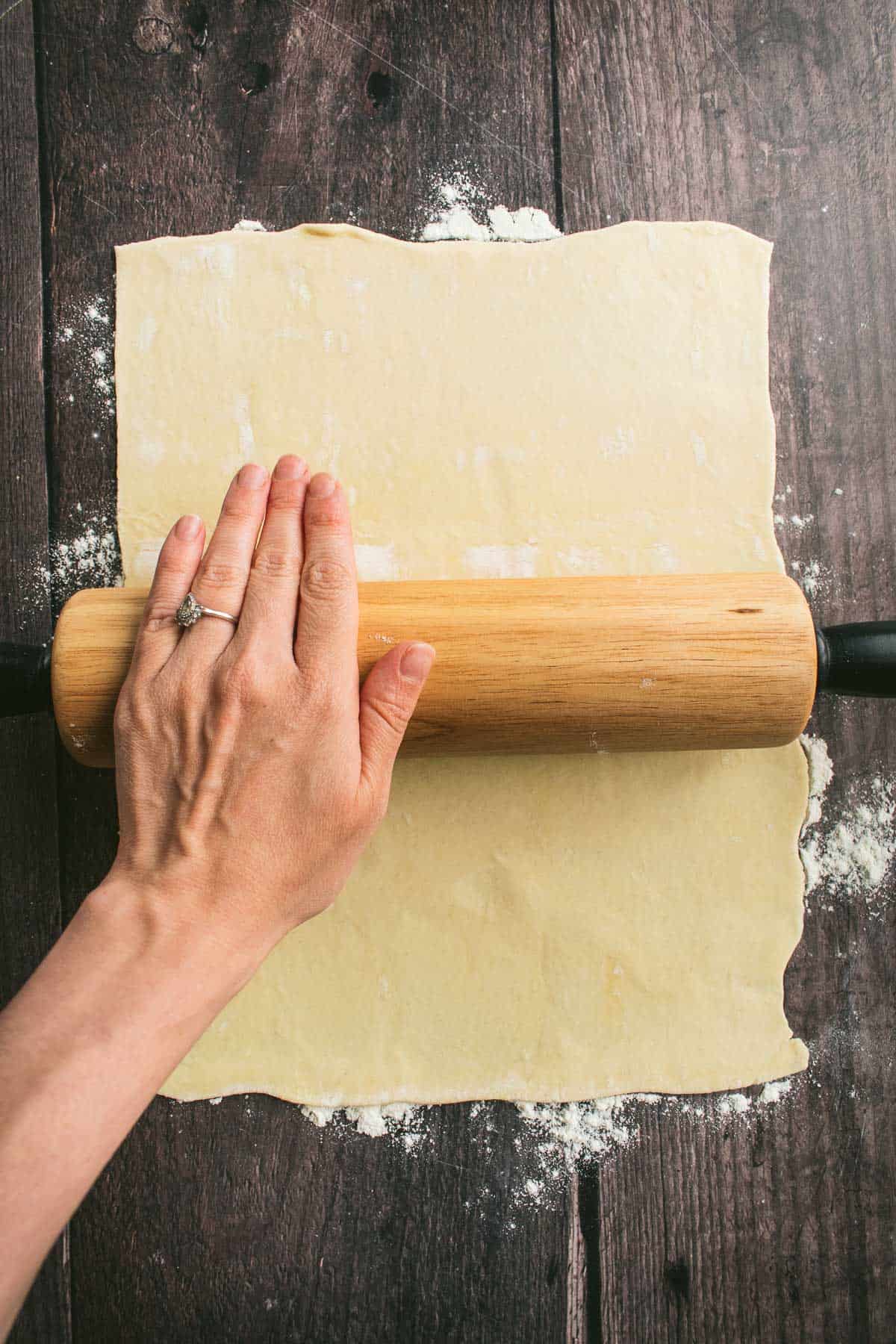 A hand rolling out puff pastry dough.