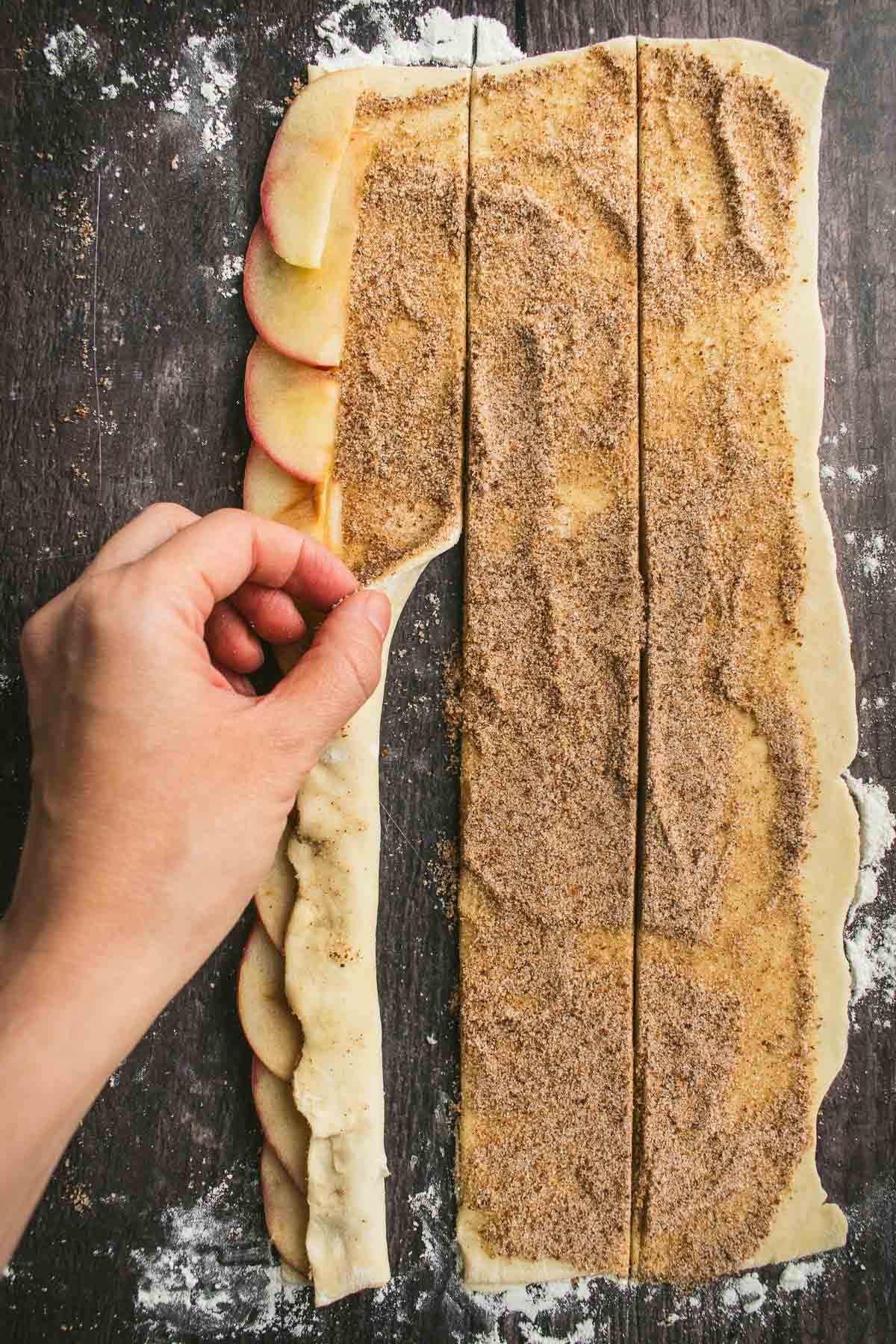 A hand folding pastry dough over apple slices.