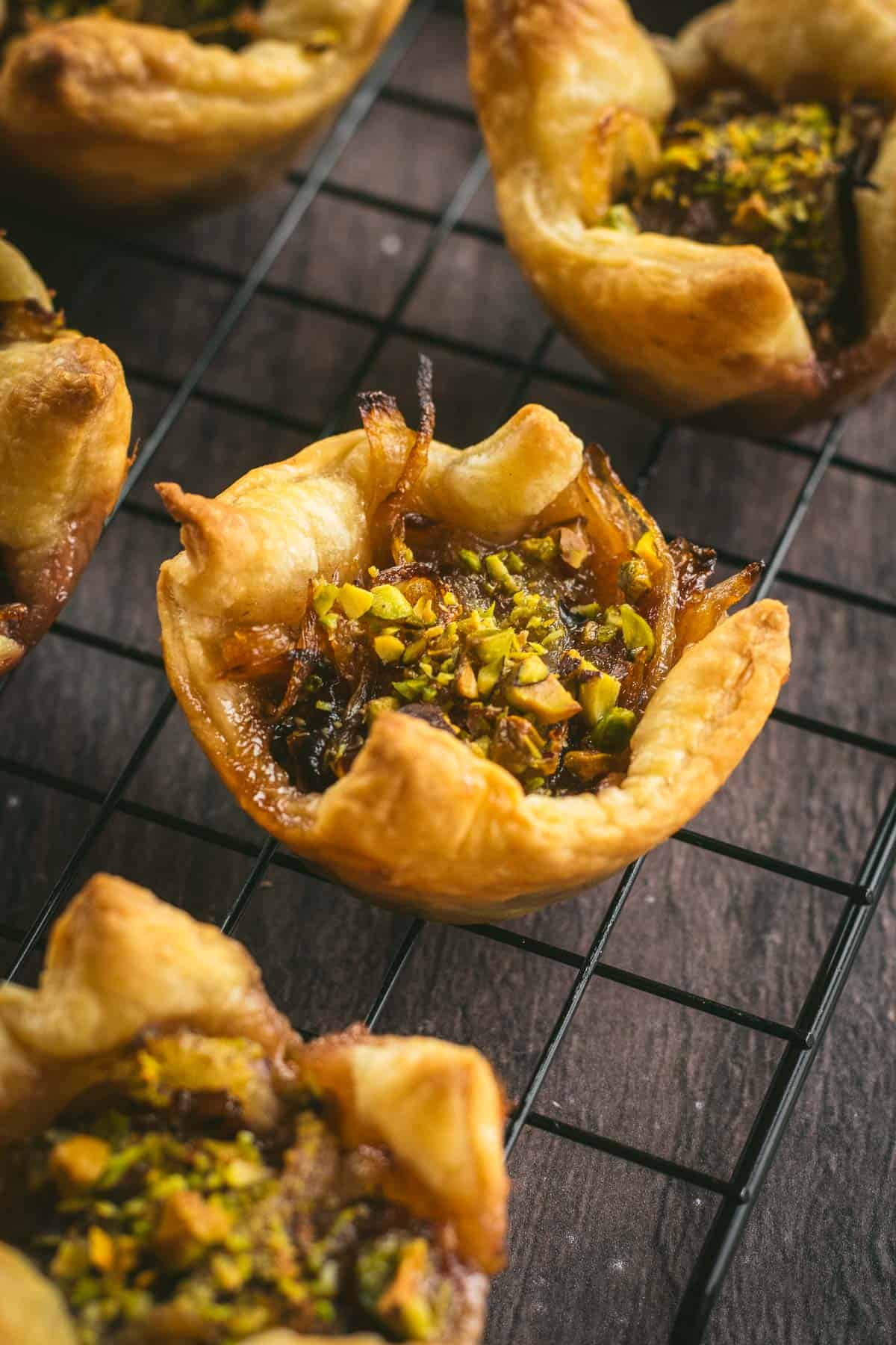 Half a dozen puff pastries on a cooling rack topped with pistachios. 