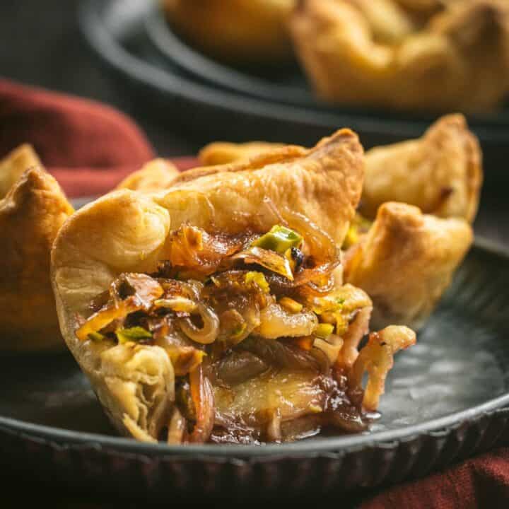 A cheese and onion puff pastry cup cut in half on a metal plate.