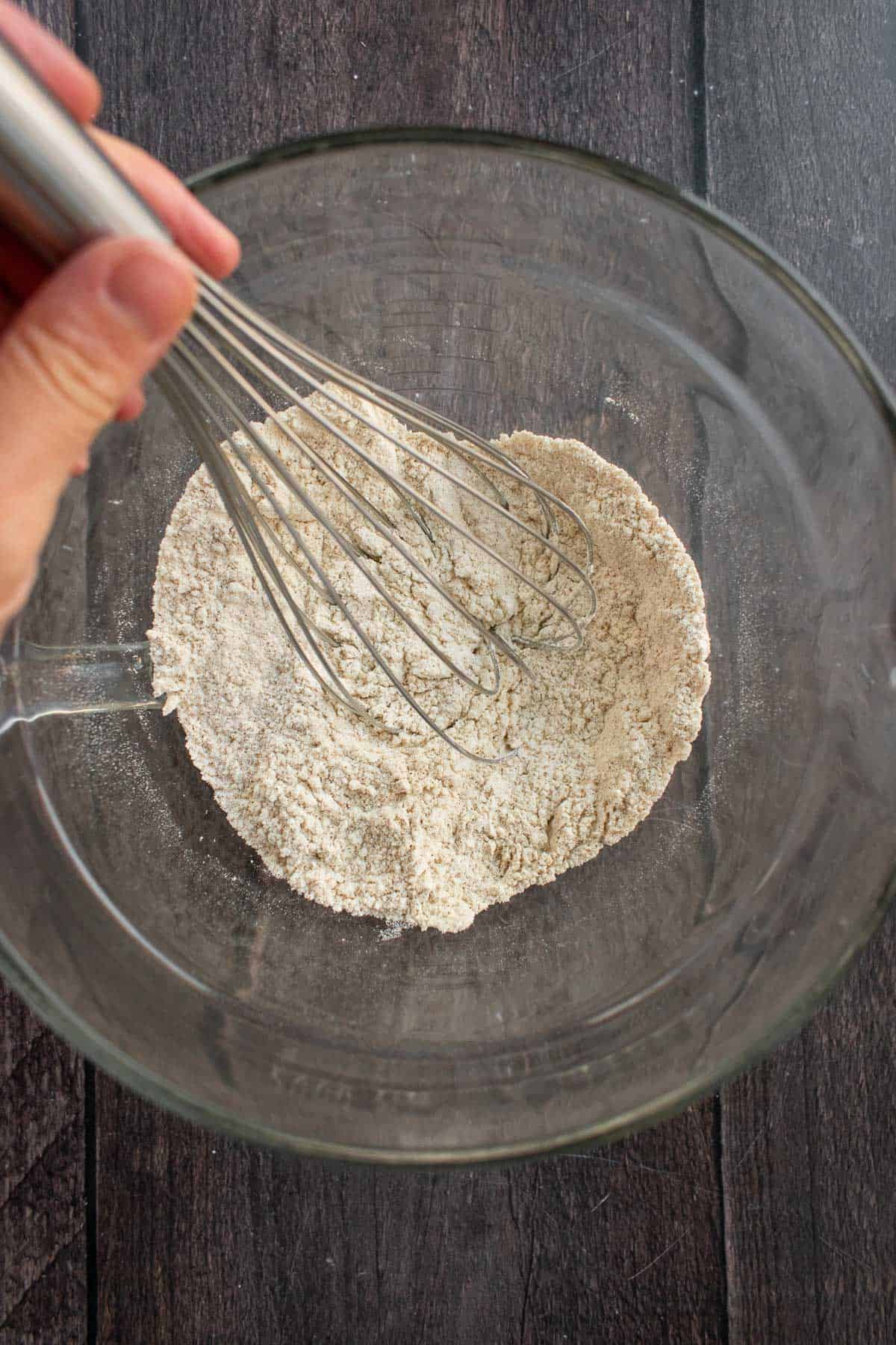 Flour, spices, baking powder, and baking soda whisked in a glass bowl.